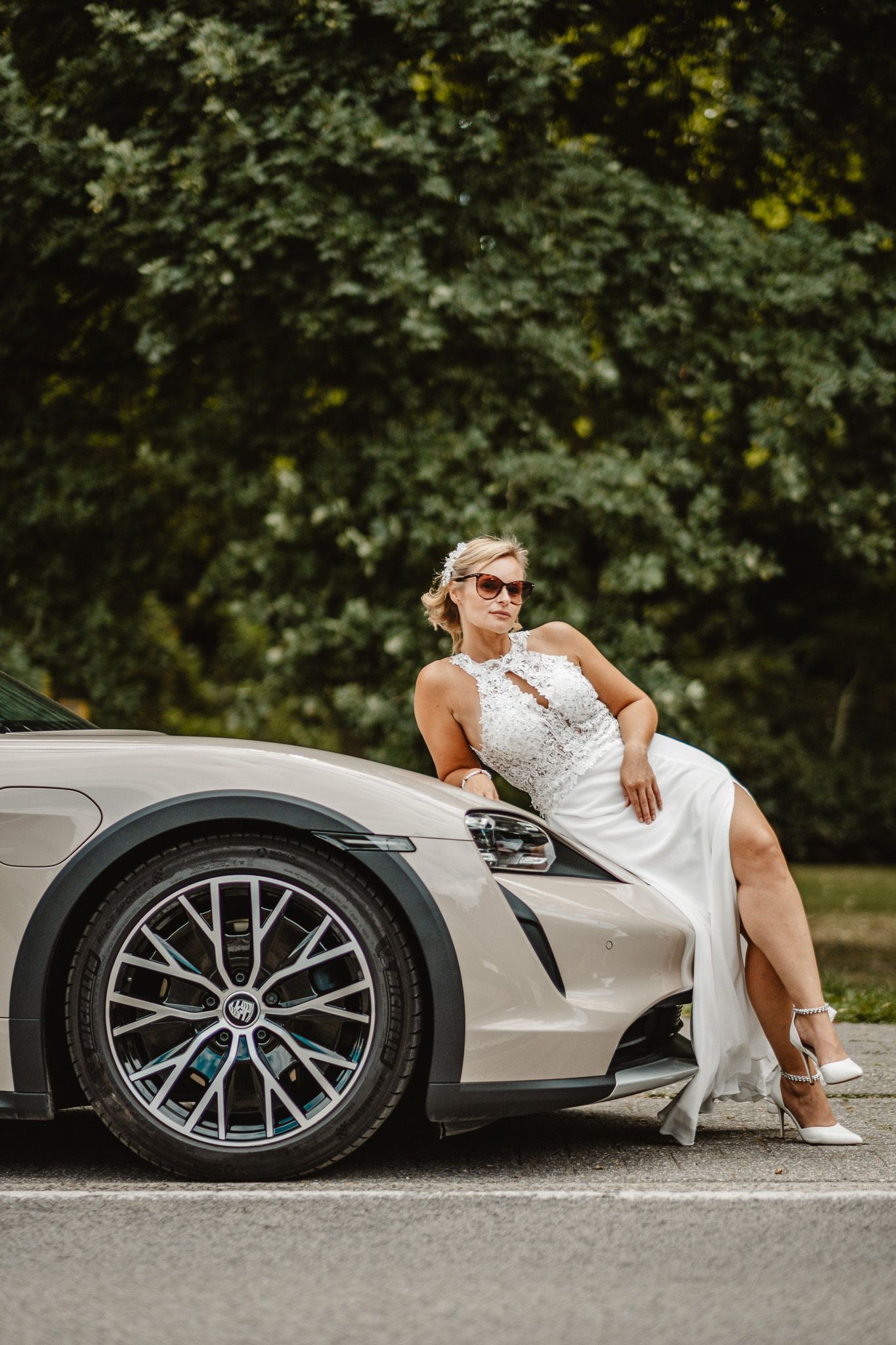 Elegant figure in white dress posed dramatically against silver sports car.