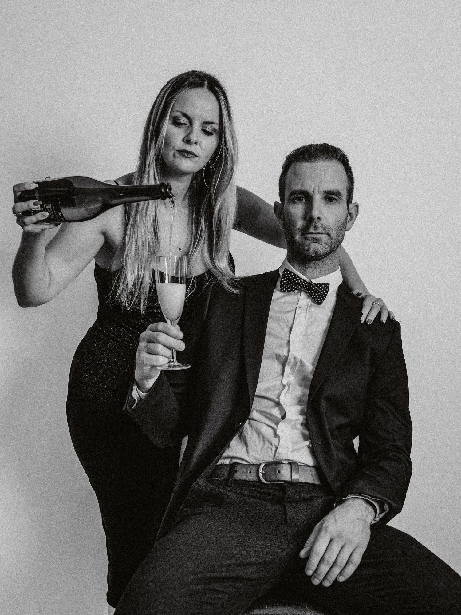 A black and white photo series showing a couple in formal attire posing intimately with wine glasses.