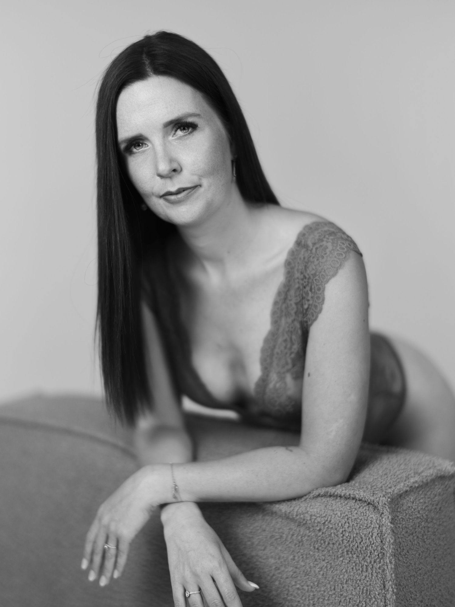 Black and white portrait of a dark-haired woman in lace lingerie posing elegantly on a couch.