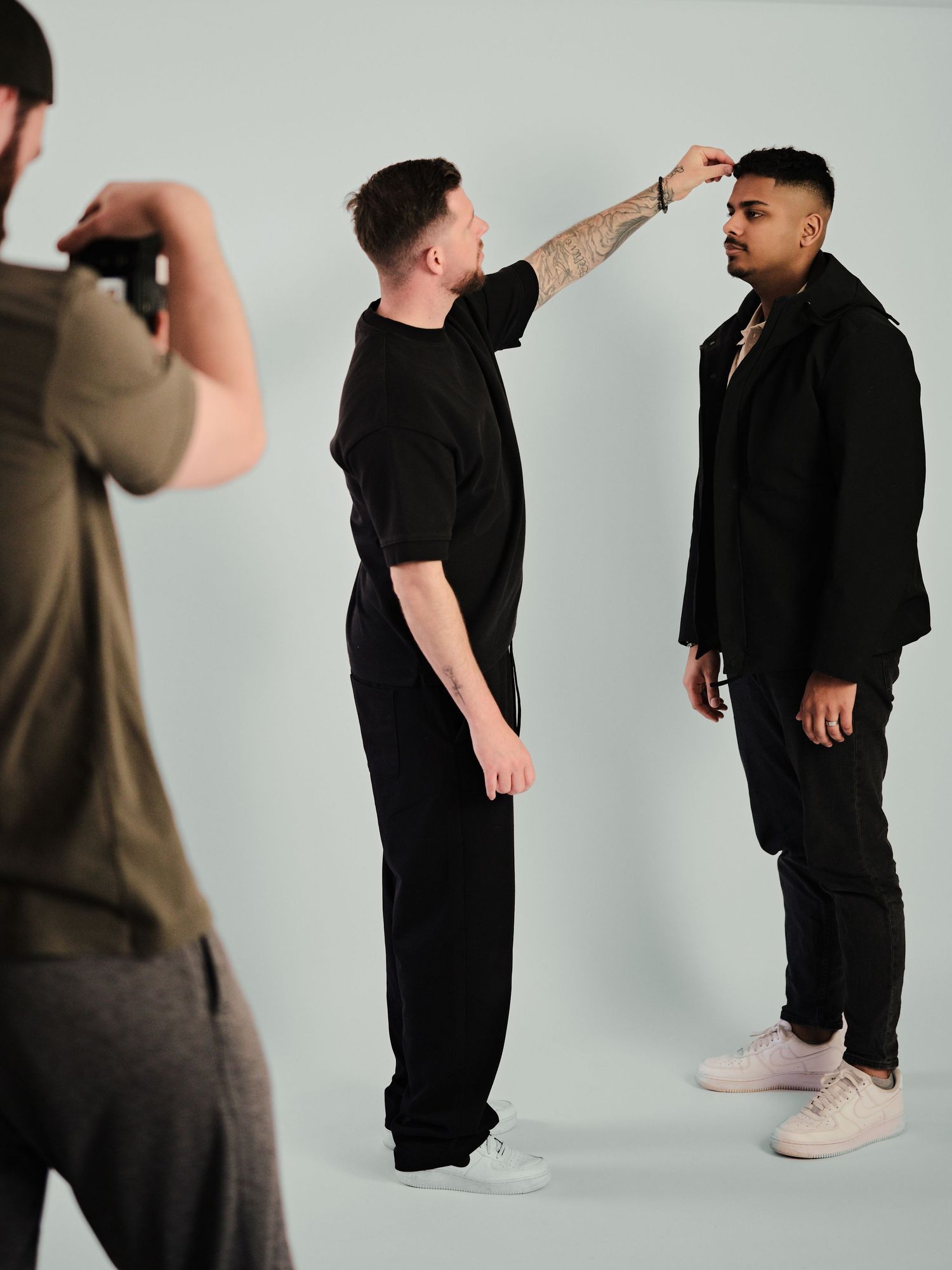 A makeup artist applies finishing touches to a male model during a professional photo shoot in a studio.