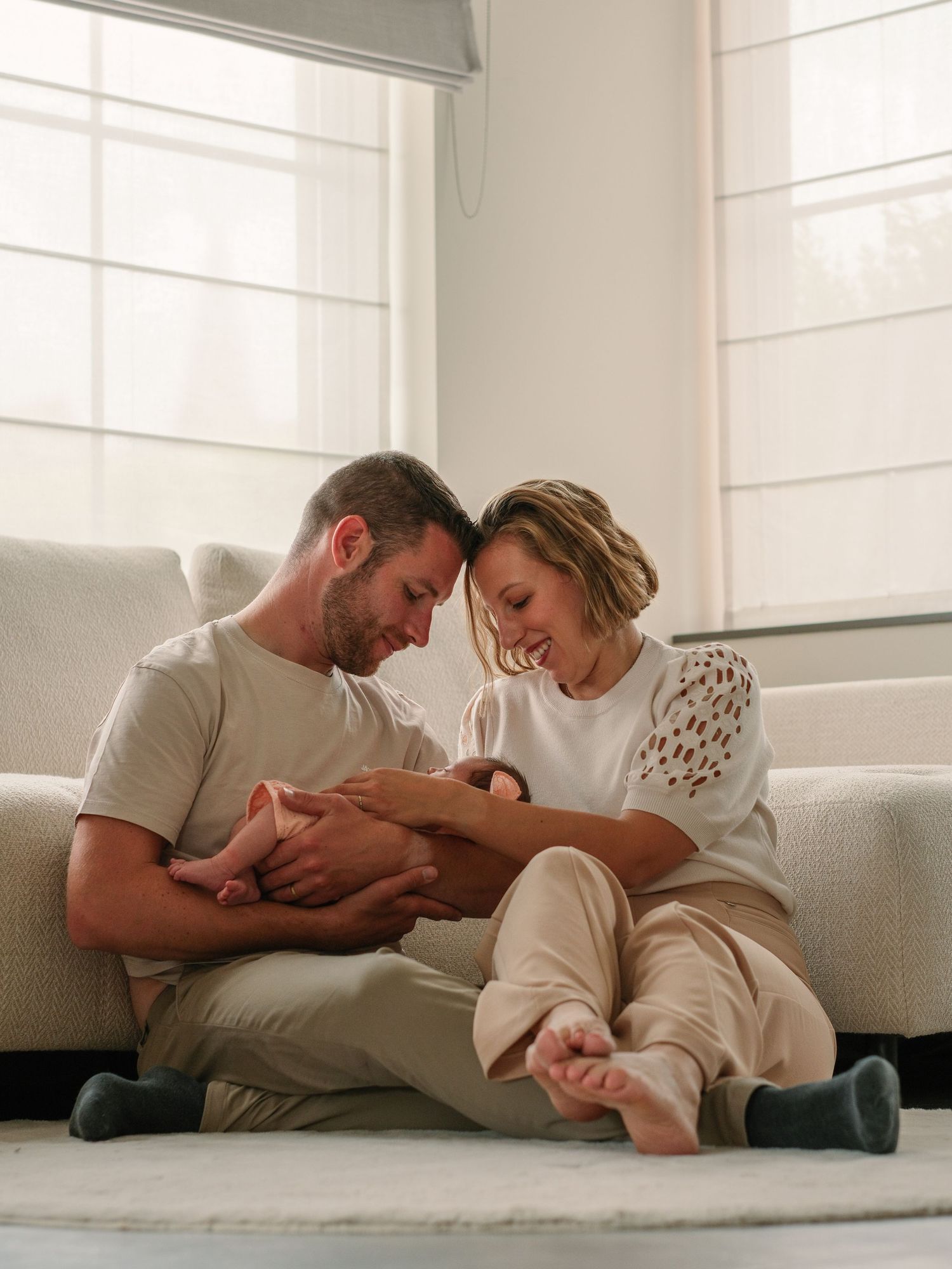 Family lounging together on white couch in bright sunlit room.