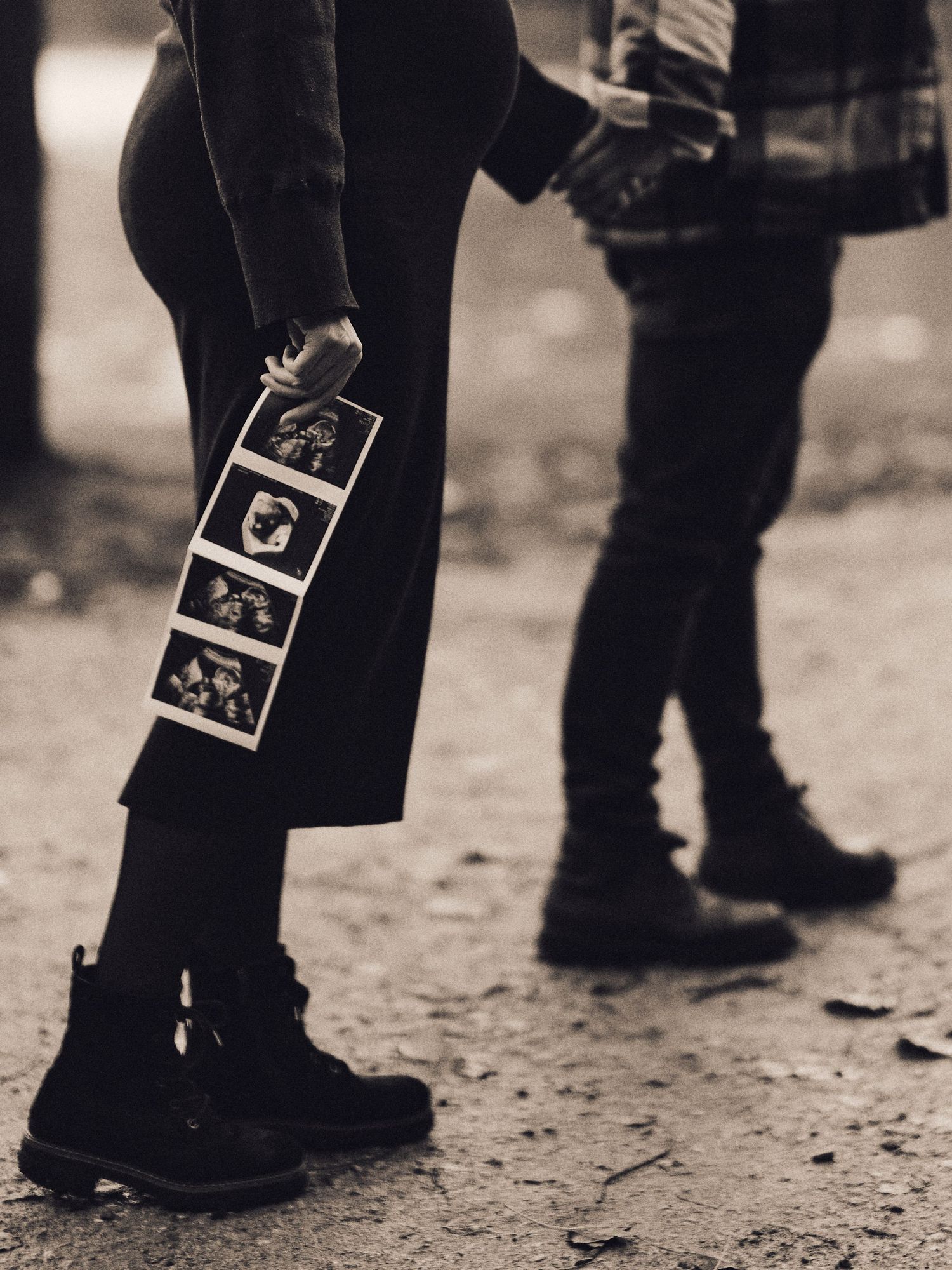 Black and white photo of legs wearing combat boots with photo strips attached to dark pants.