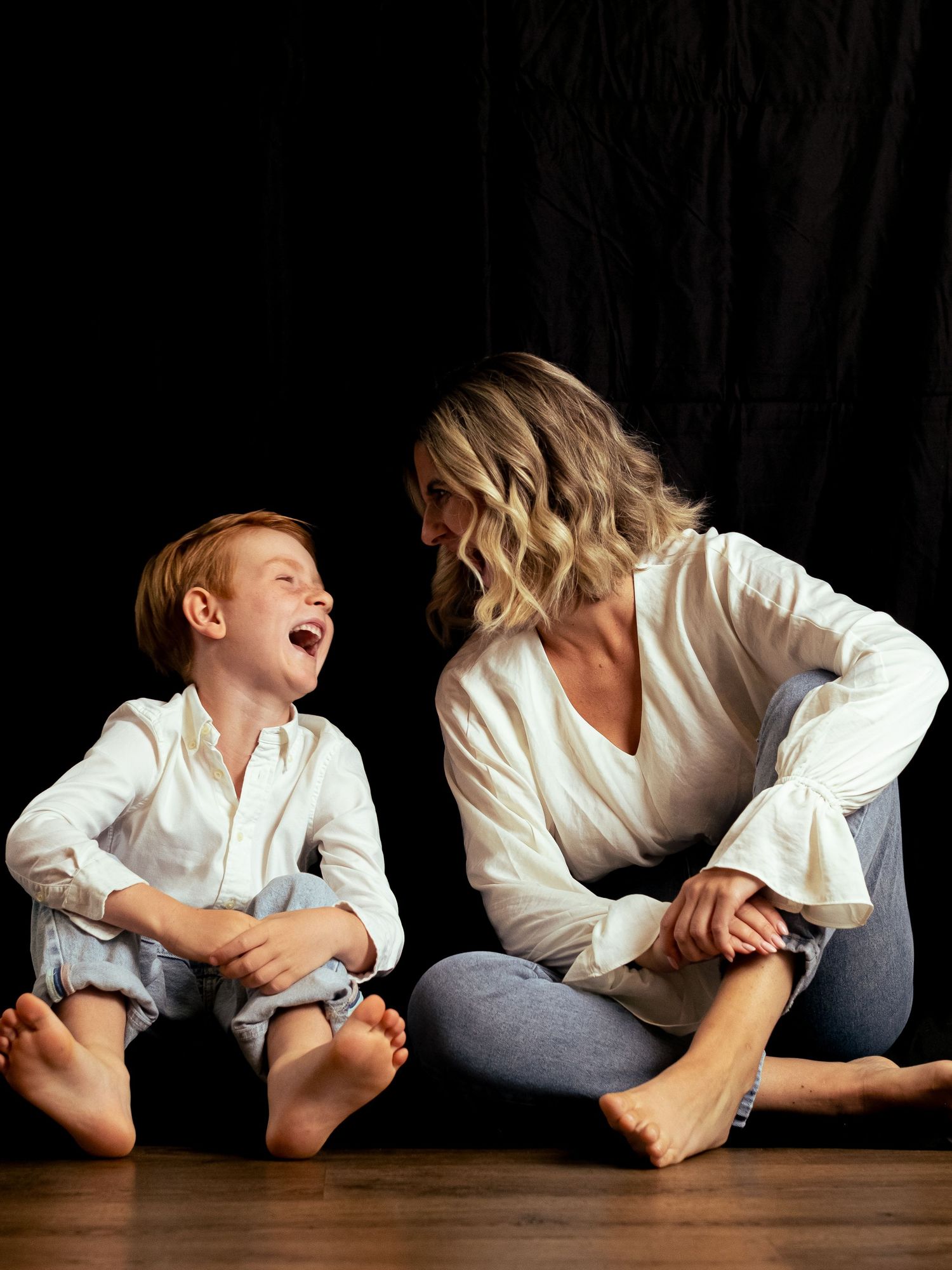 Playful lifestyle portrait session with subjects lying on dark floor in white shirts.