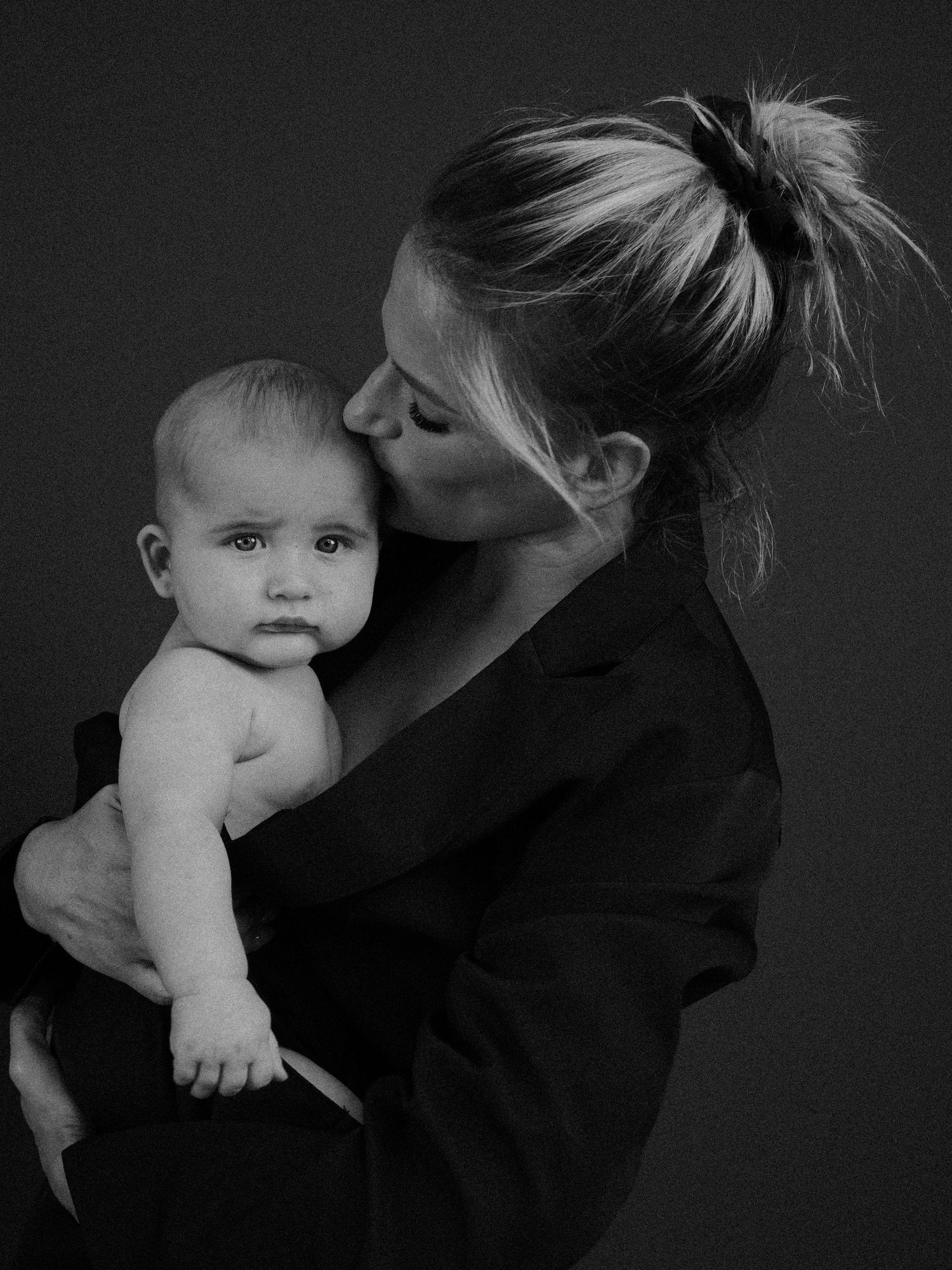 A tender black and white portrait of a parent giving a gentle kiss to their baby in an intimate studio setting.