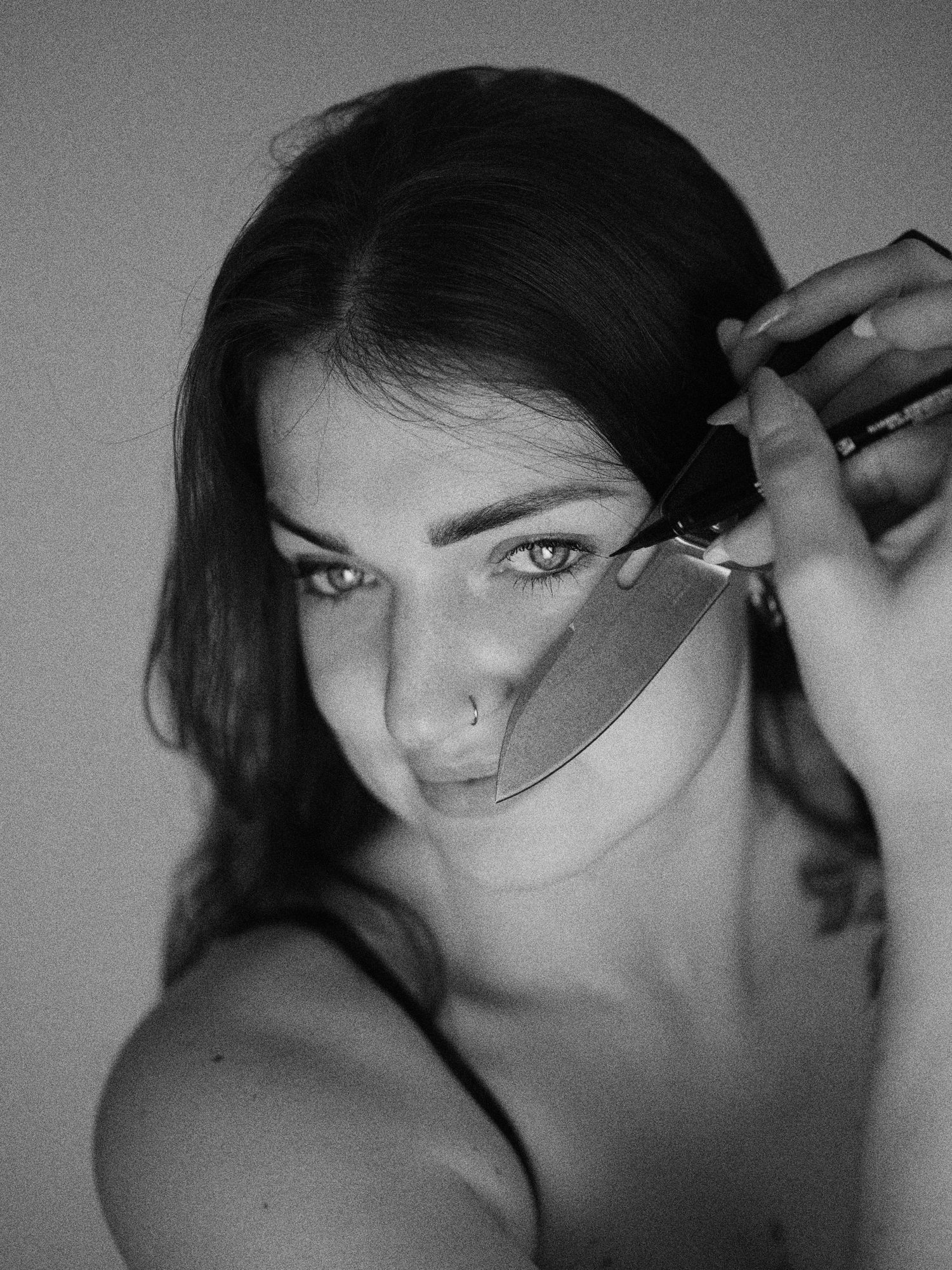 Black and white portrait of a young woman holding a knife near her face, dramatic artistic photography.