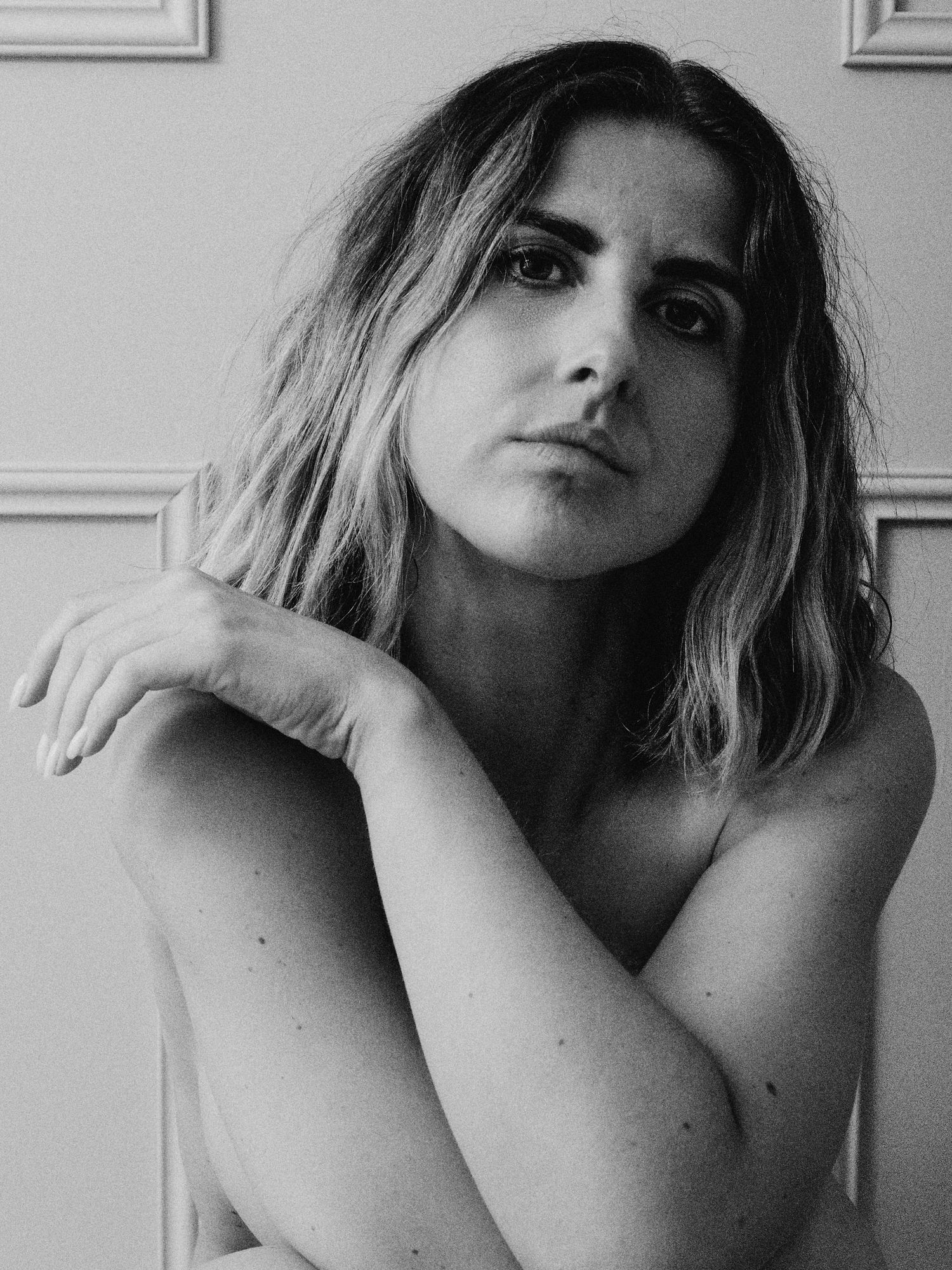 Black and white portrait of a young woman with shoulder-length hair posing thoughtfully with arms crossed.