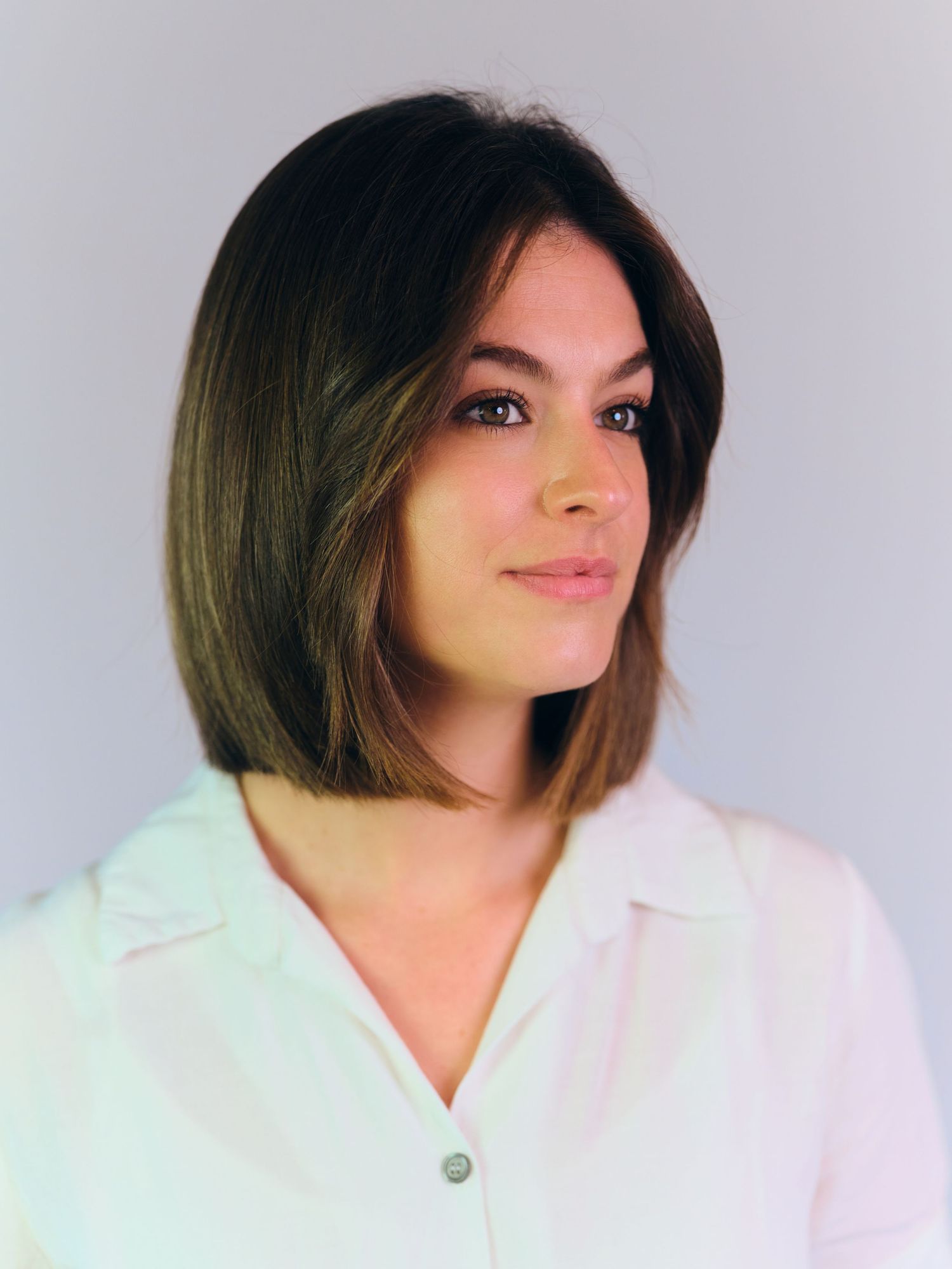 Professional headshot of a young woman with a dark bob hairstyle wearing a white blouse against a light gray background.