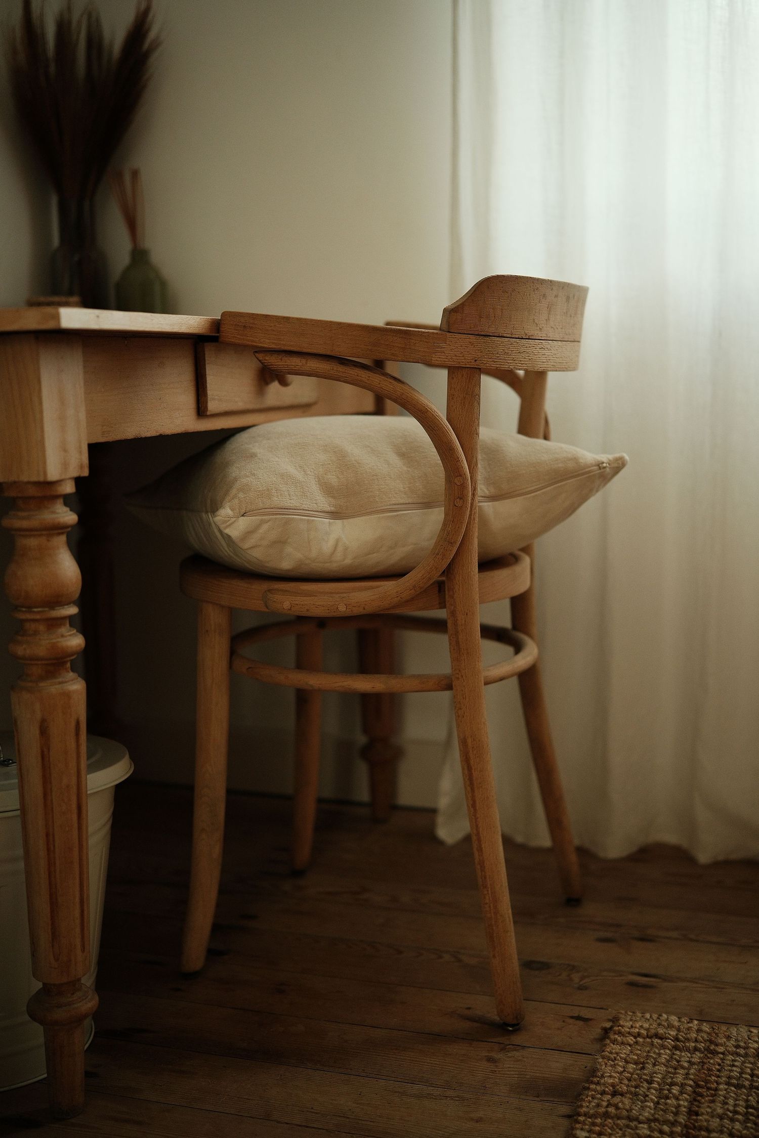 Rustic wooden chairs and table against white curtained window.