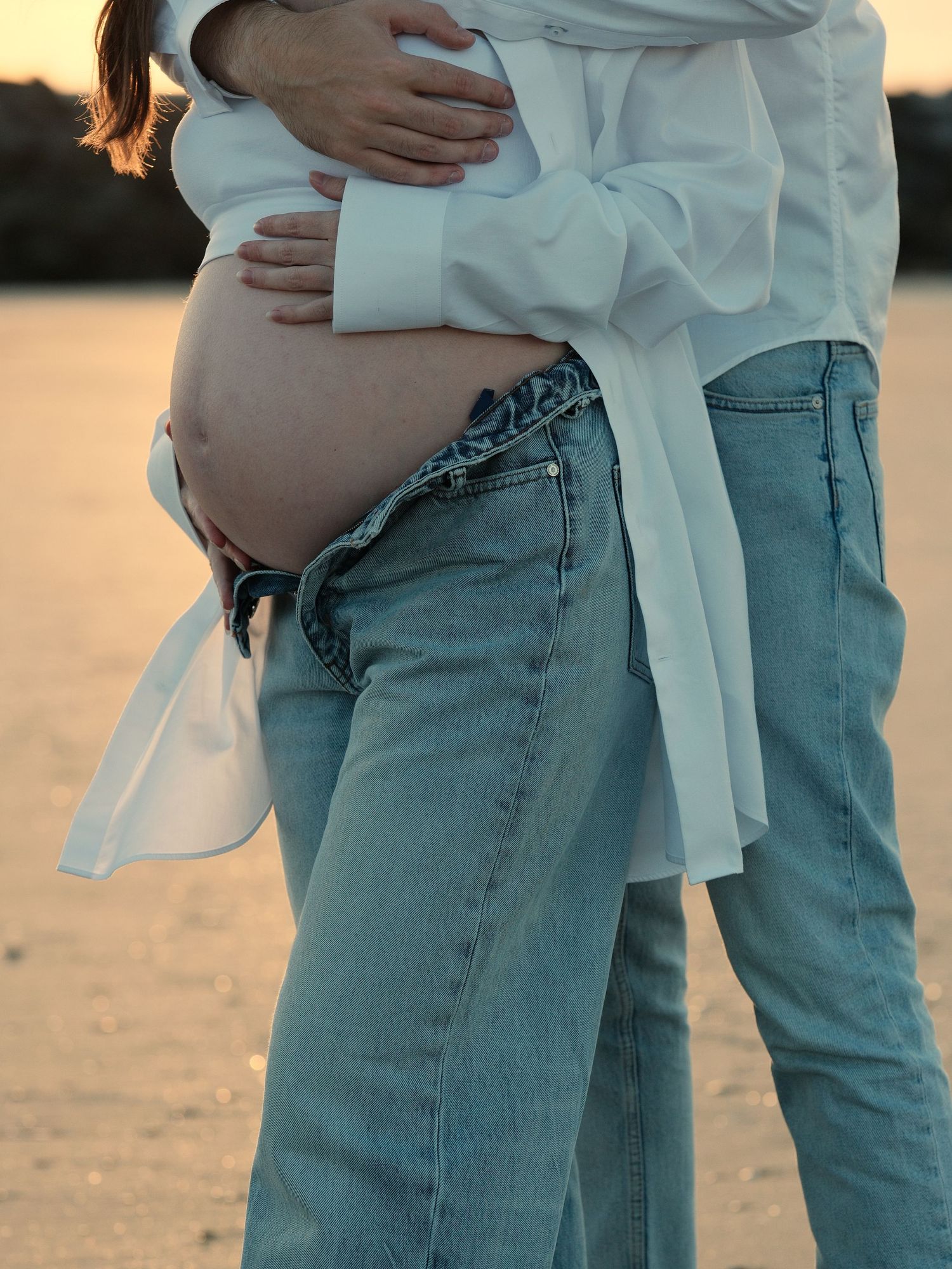 Casual maternity photos showing denim and white shirt combination in warm light.