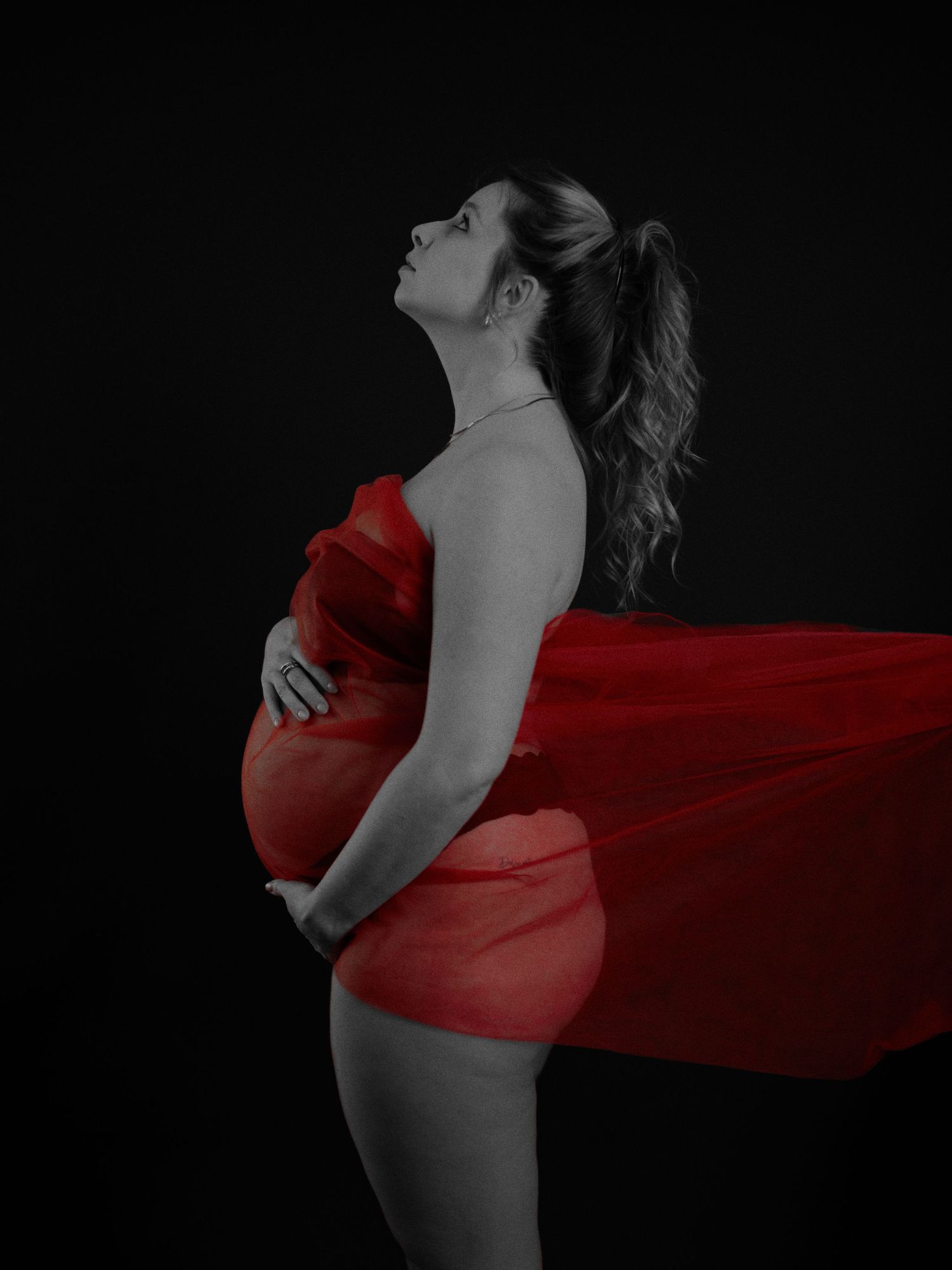 A figure in red fabric poses dramatically against a black background creating an artistic silhouette effect.