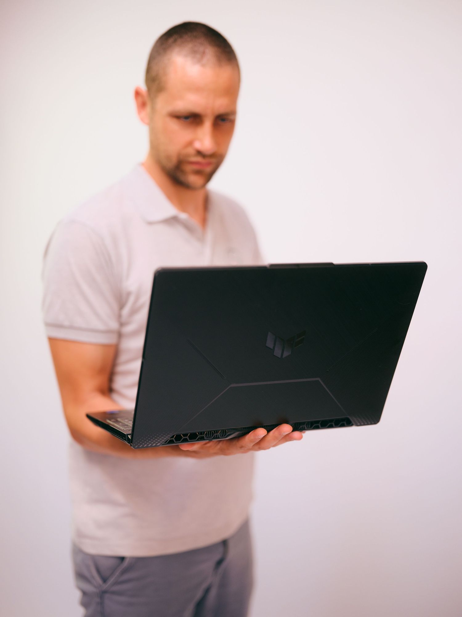 Man holding an open ASUS TUF gaming laptop, viewed from behind, against a white background.