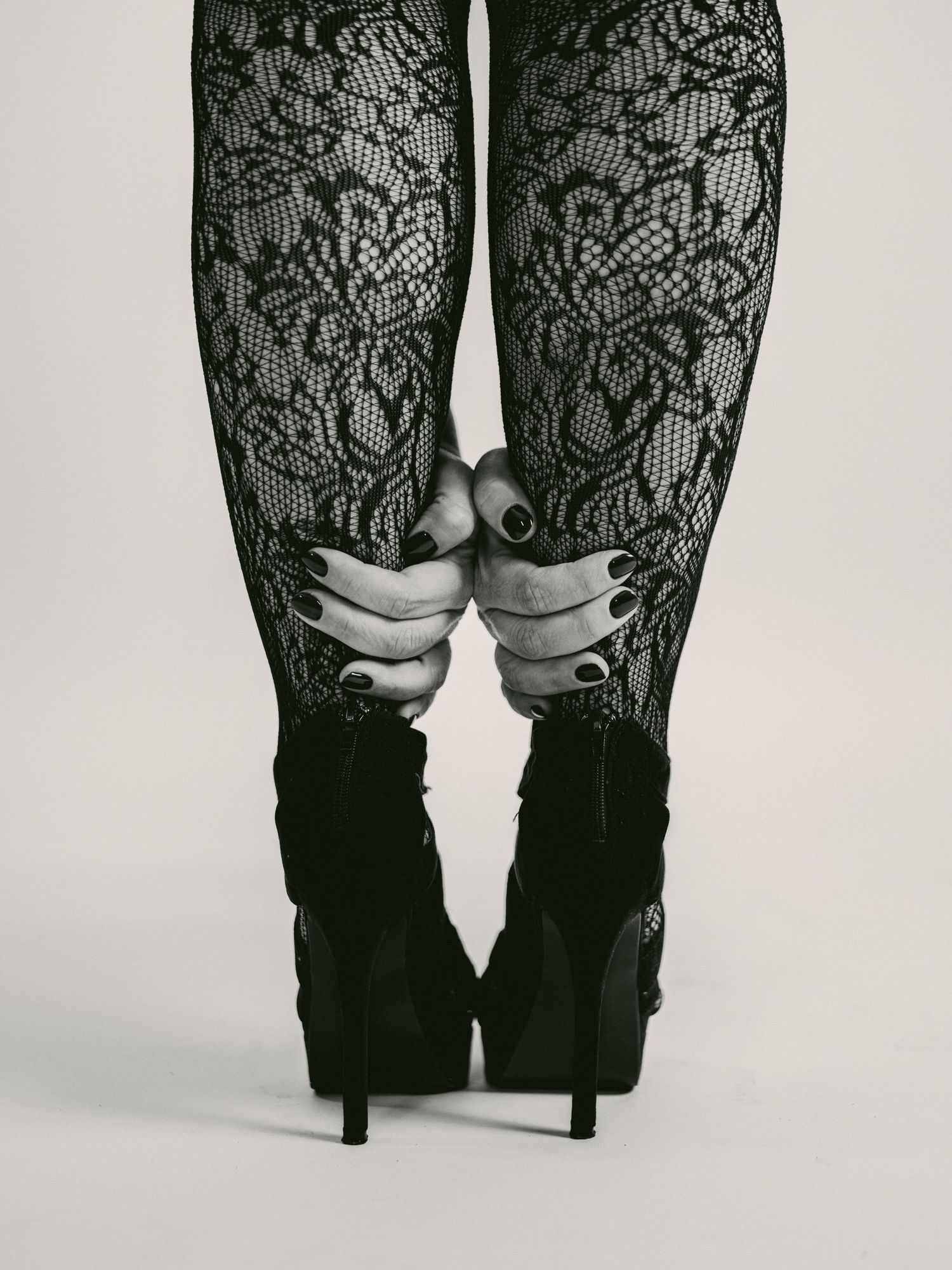 Close-up view of black lace stockings paired with high heel ankle boots in a fashion-forward style.