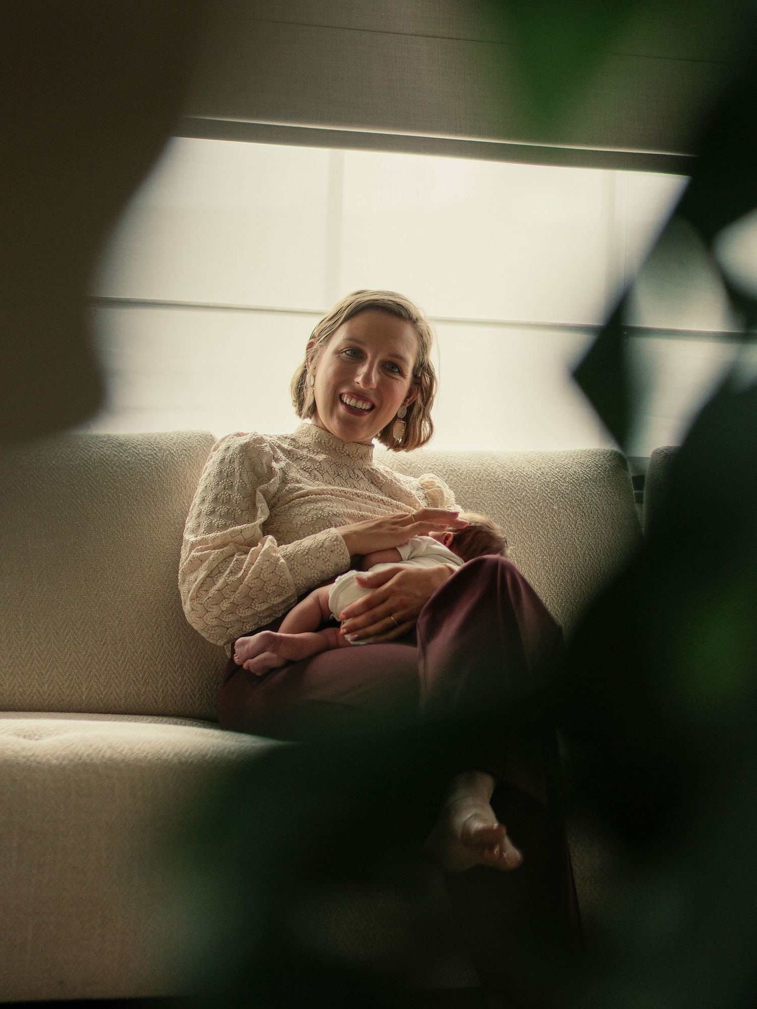Person in a cream sweater relaxes on a white couch in soft natural lighting.