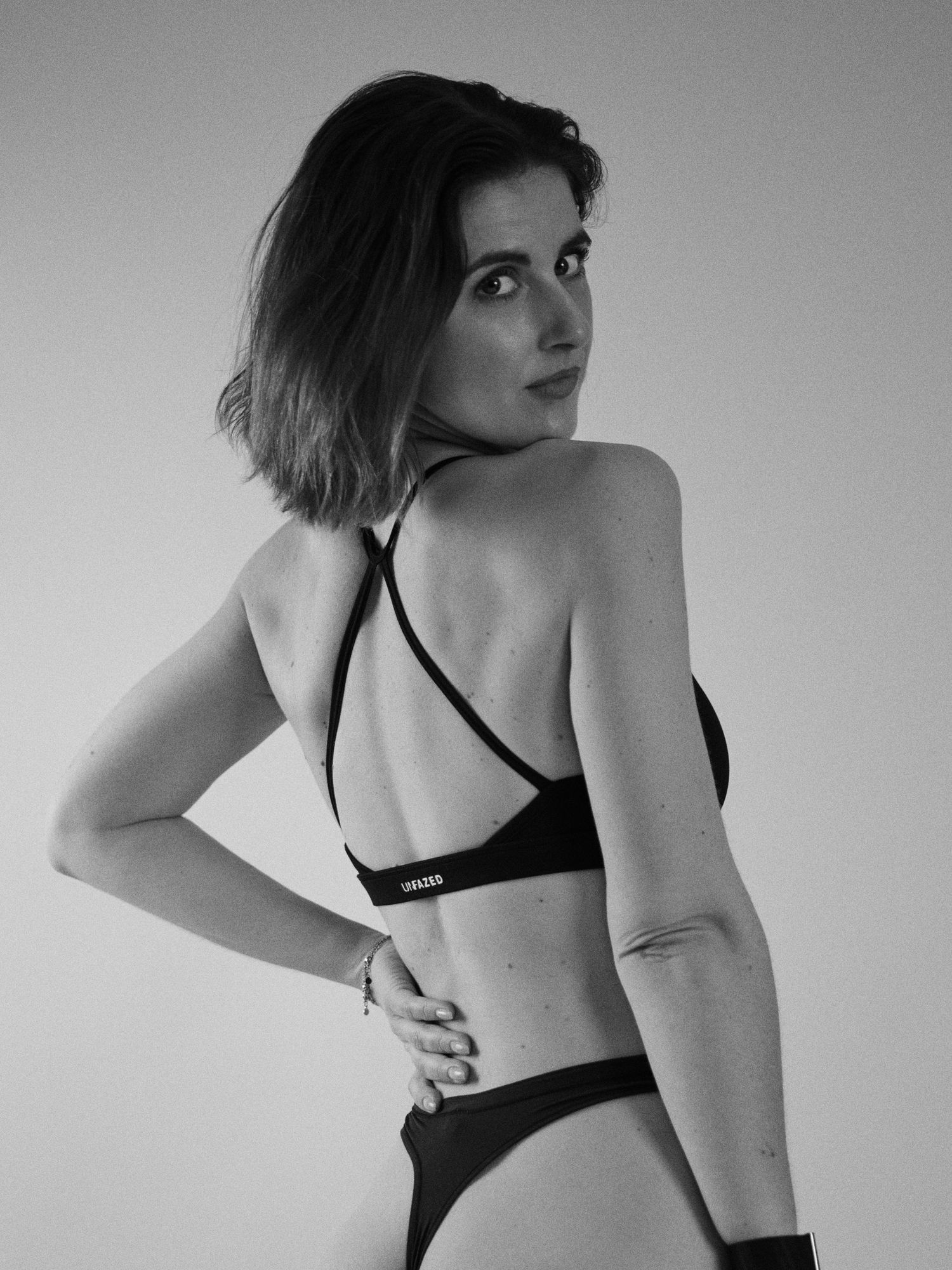 Black and white photo of a woman in a black bikini posing with her back to the camera.