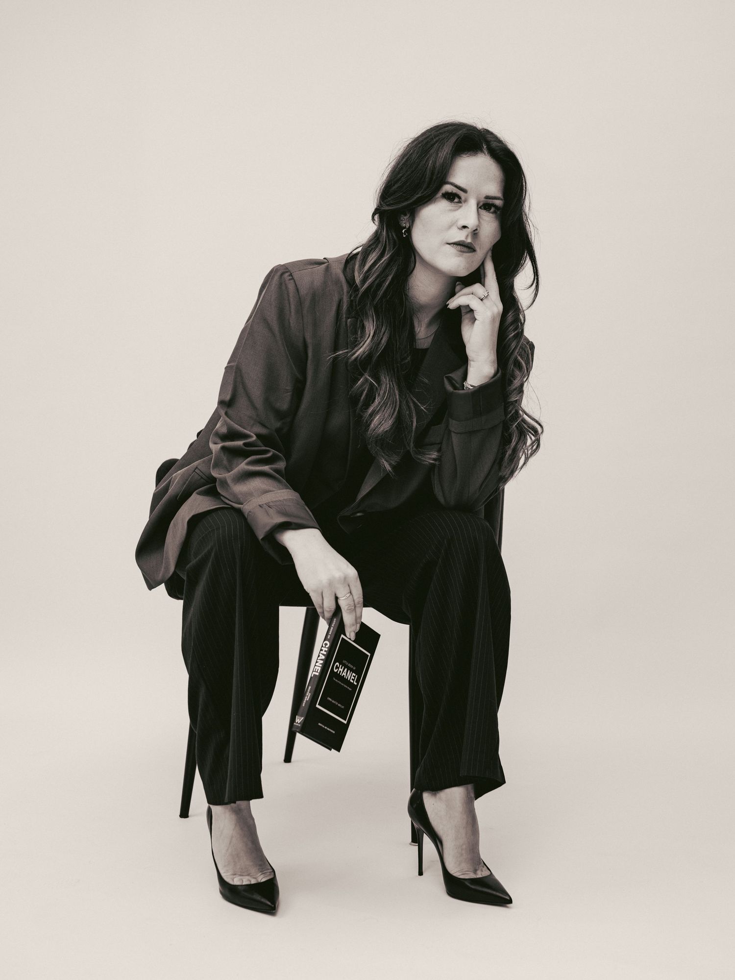 A series of black and white fashion portraits showing a person in dark business attire posing in various contemplative stances.