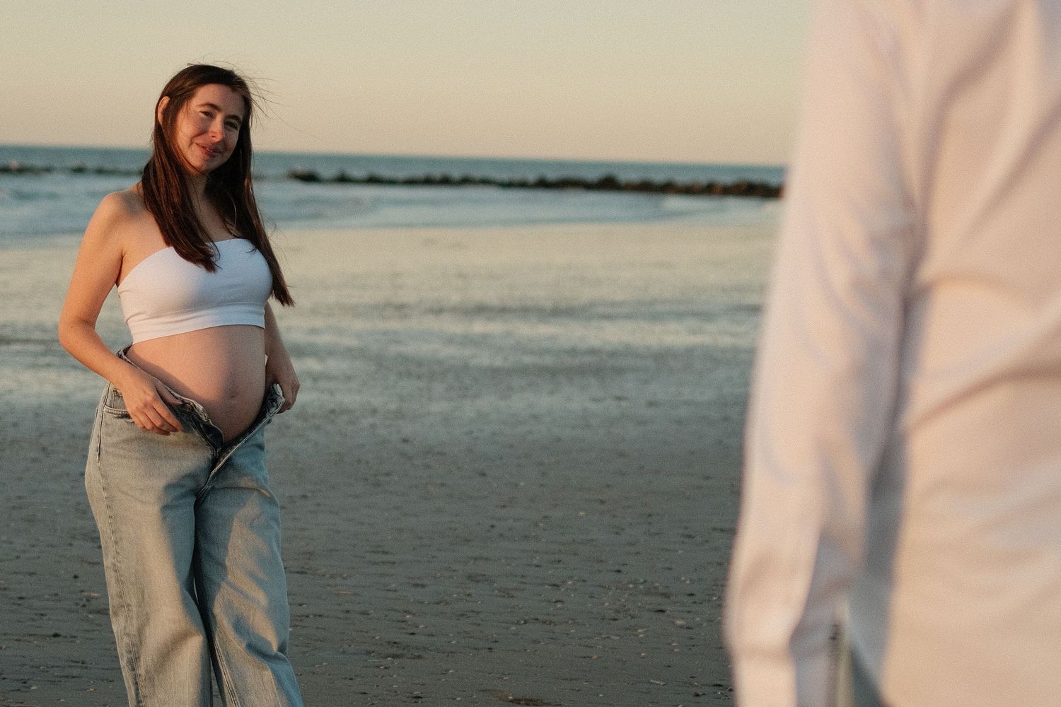 Beachside maternity photos with couple in casual white and denim attire.