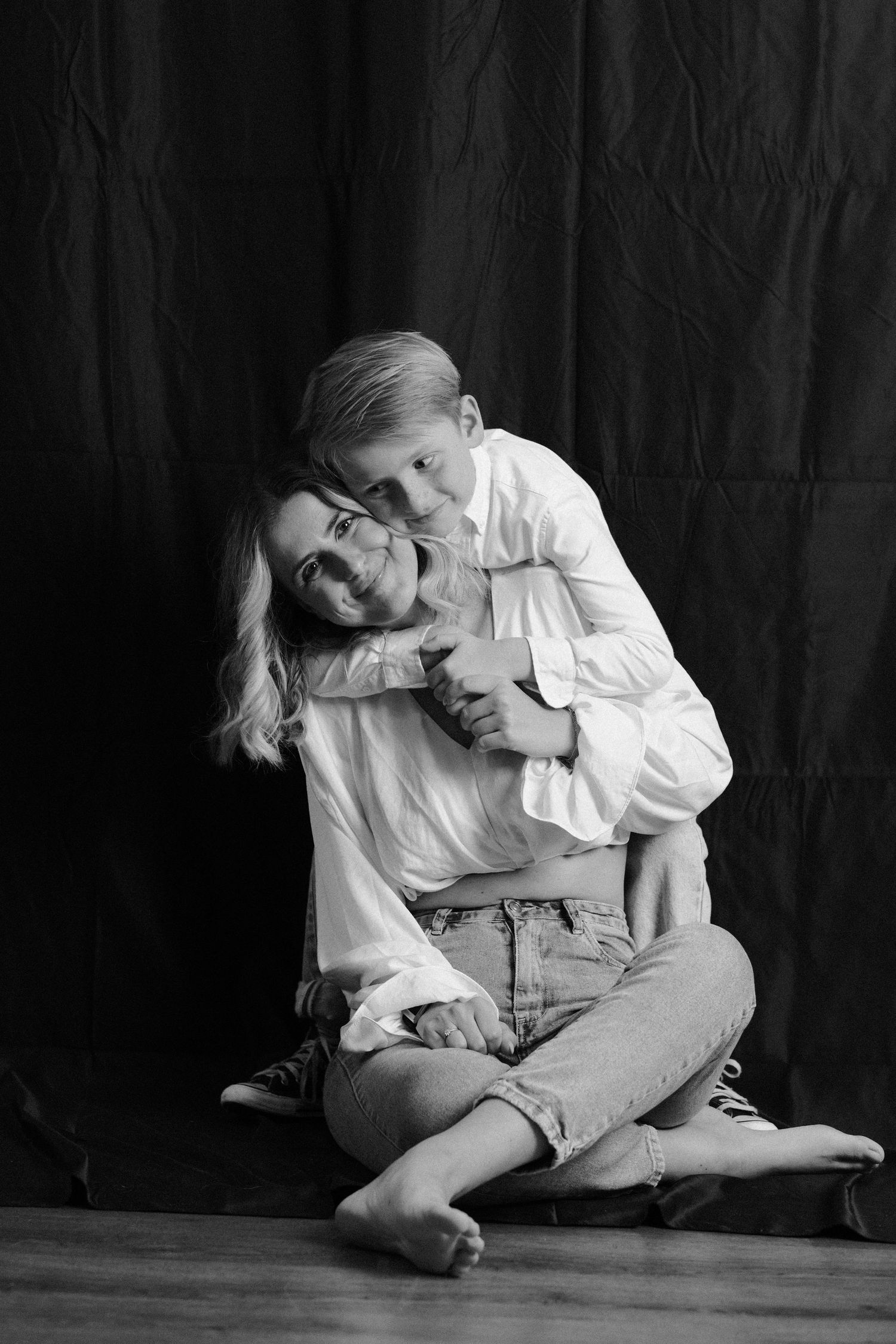 Artistic black and white portrait series showing person in white clothing sitting on dark floor.