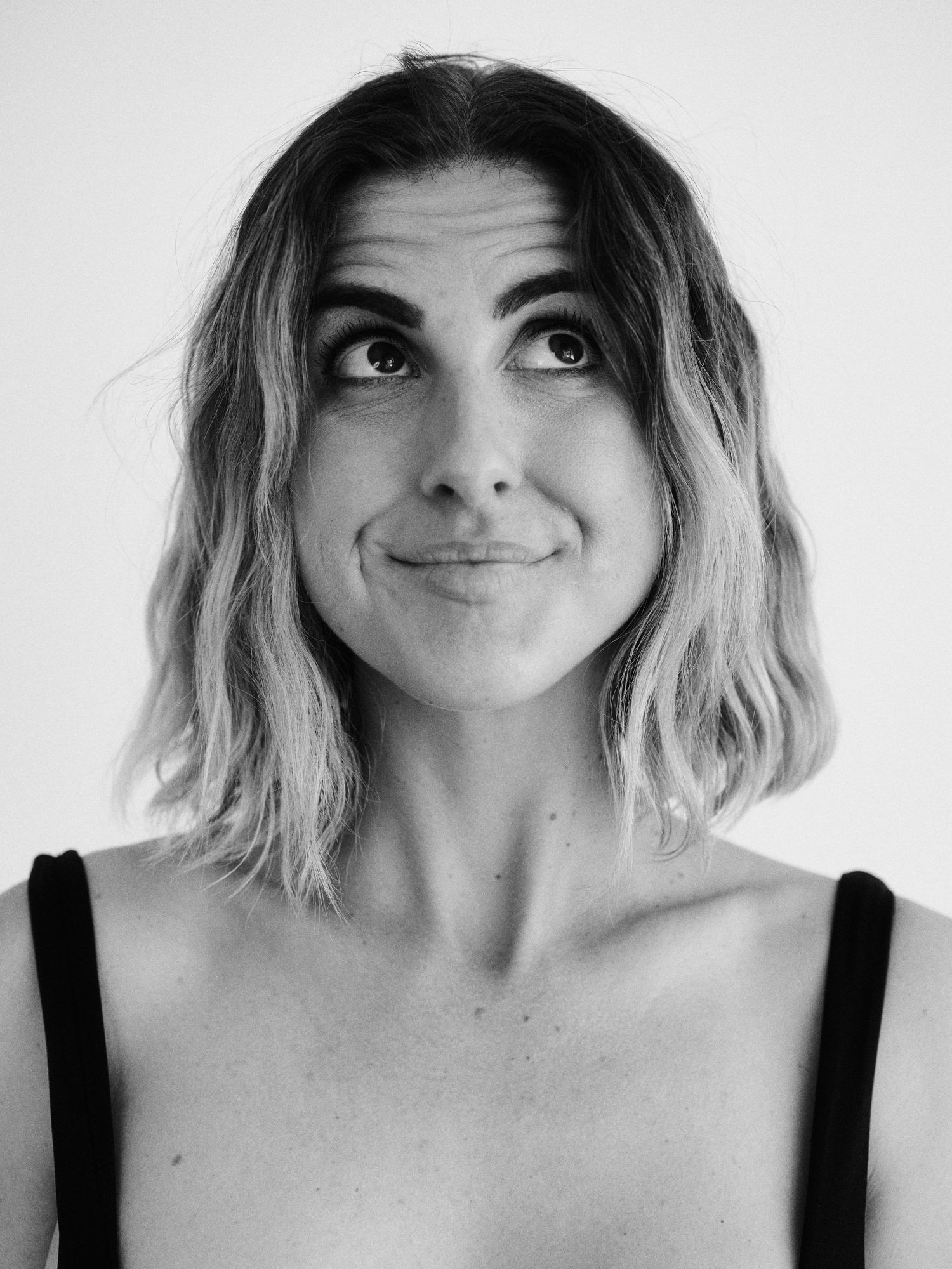 Black and white portrait of a young woman with wavy bob hair, looking up with a playful smile.