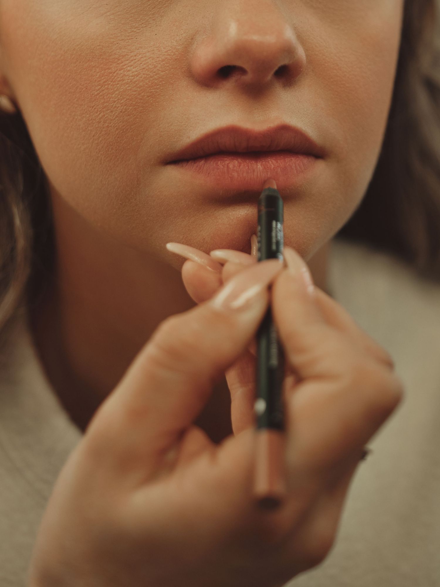 Close-up of a makeup artist applying dark lip liner pencil to a woman's full lips with precision.