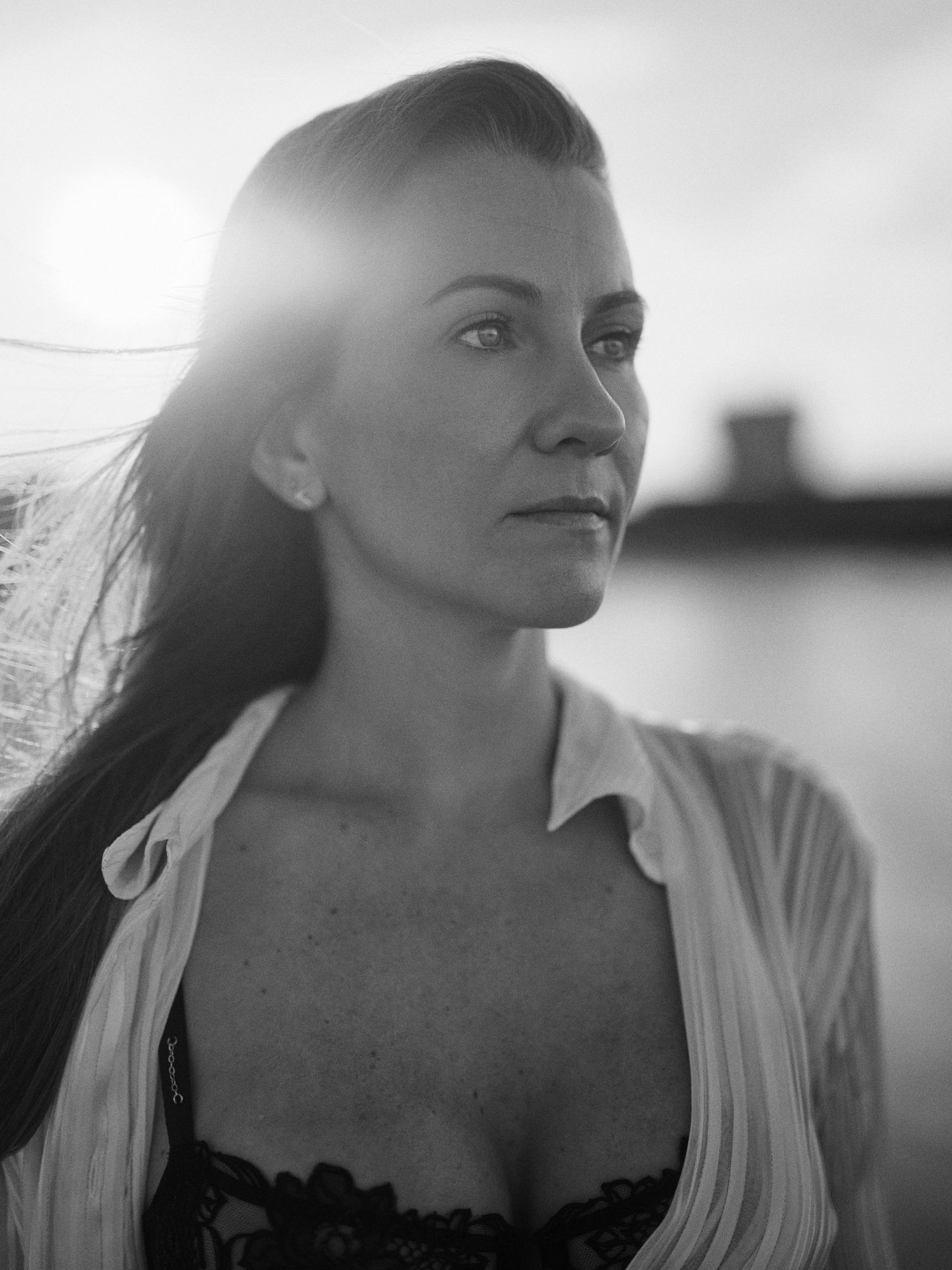 Black and white portrait of a woman with long dark hair, backlit by sunlight near water.