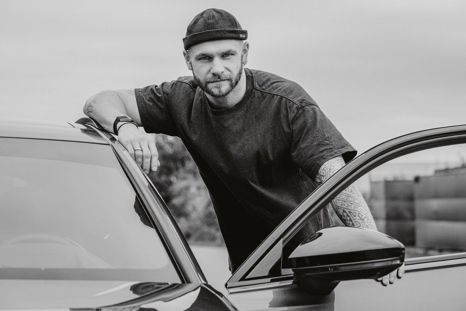 A series of black and white images showing a person working on and posing with a classic car in various angles.