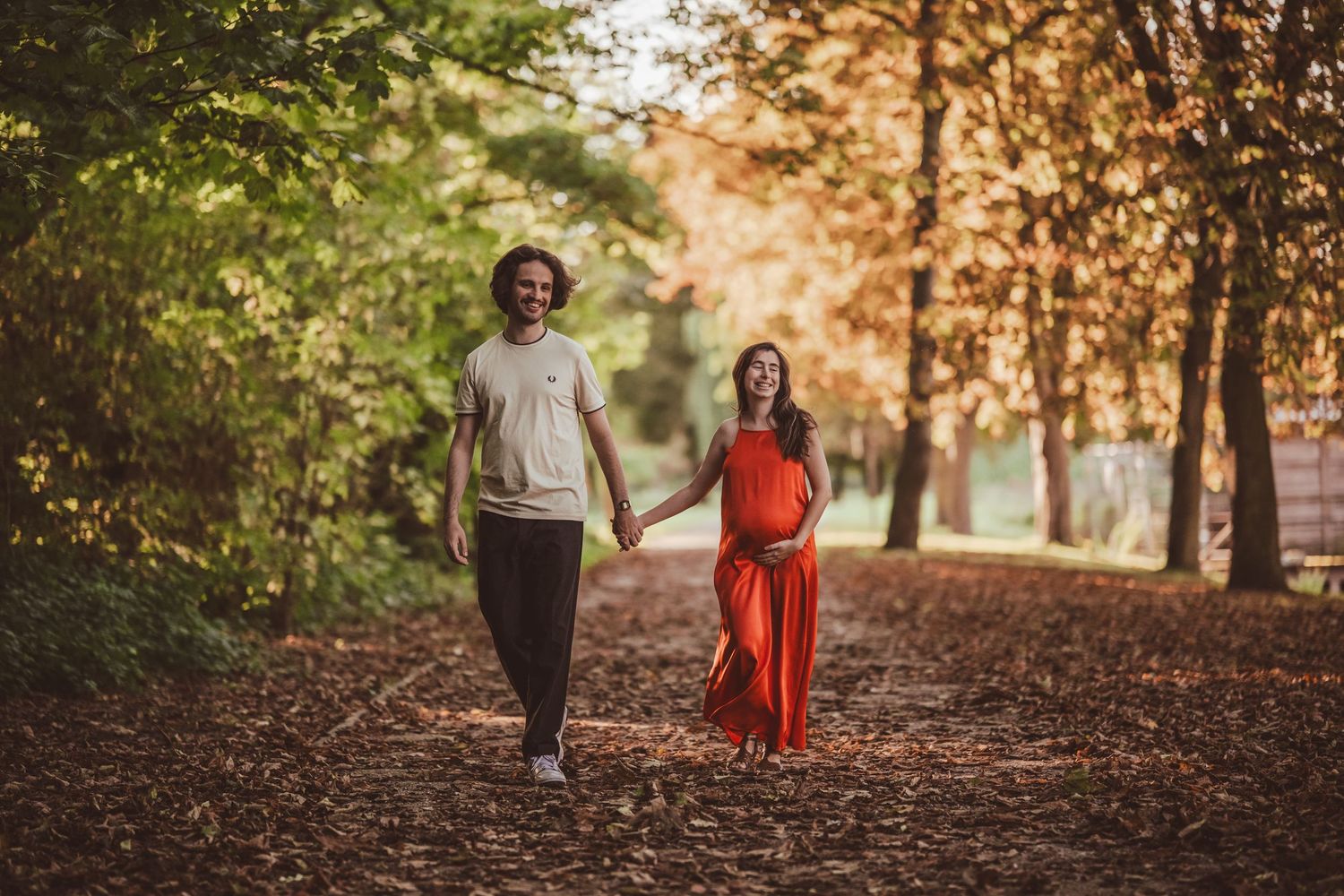 Couple walking through a wooded path during golden hour for maternity photos.