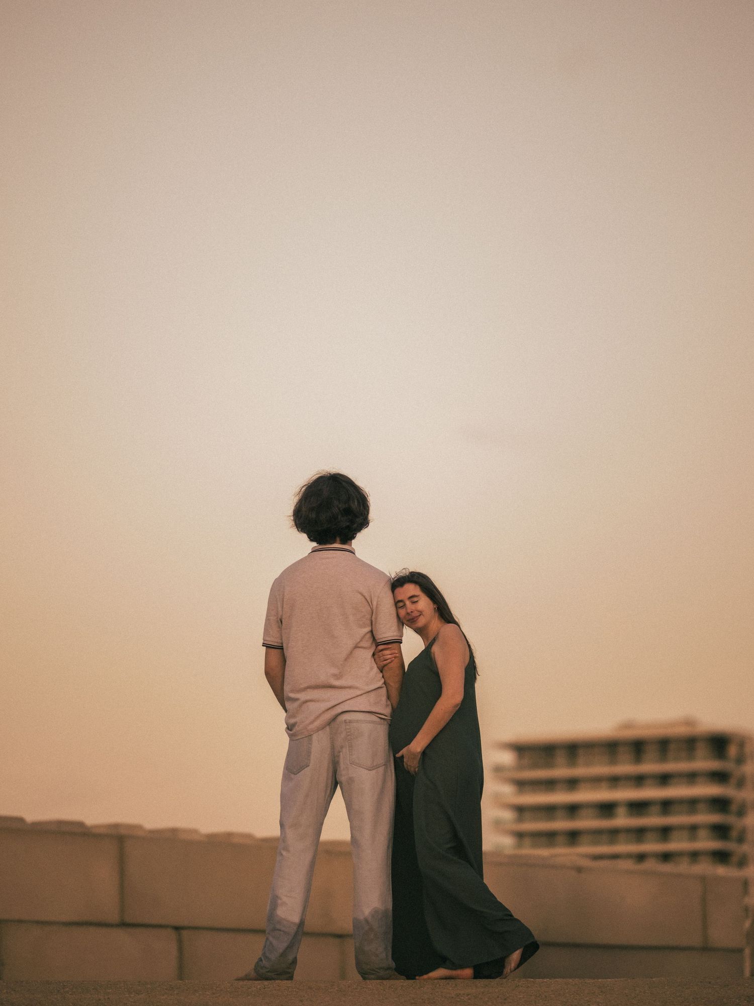 Two people sit together on a rooftop at sunset creating a romantic silhouette against the warm sky.