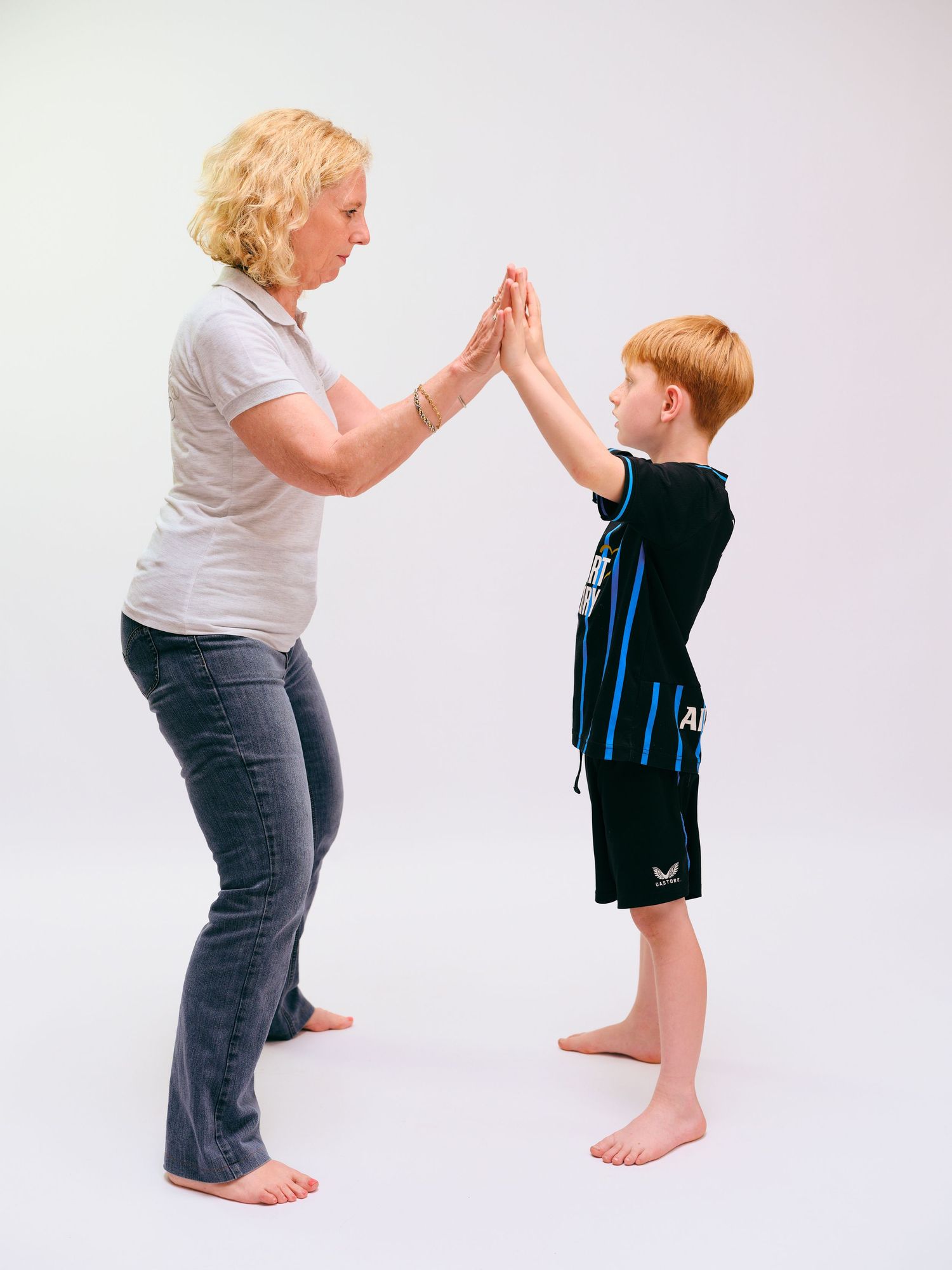Woman and red-haired boy giving high five while standing barefoot against white background.
