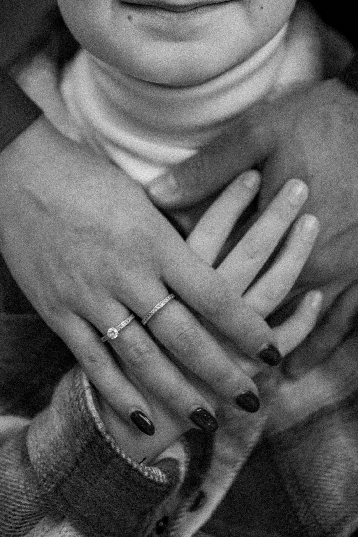 Black and white close-up sequence showing hands with dark nail polish and rings against a textured fabric background.