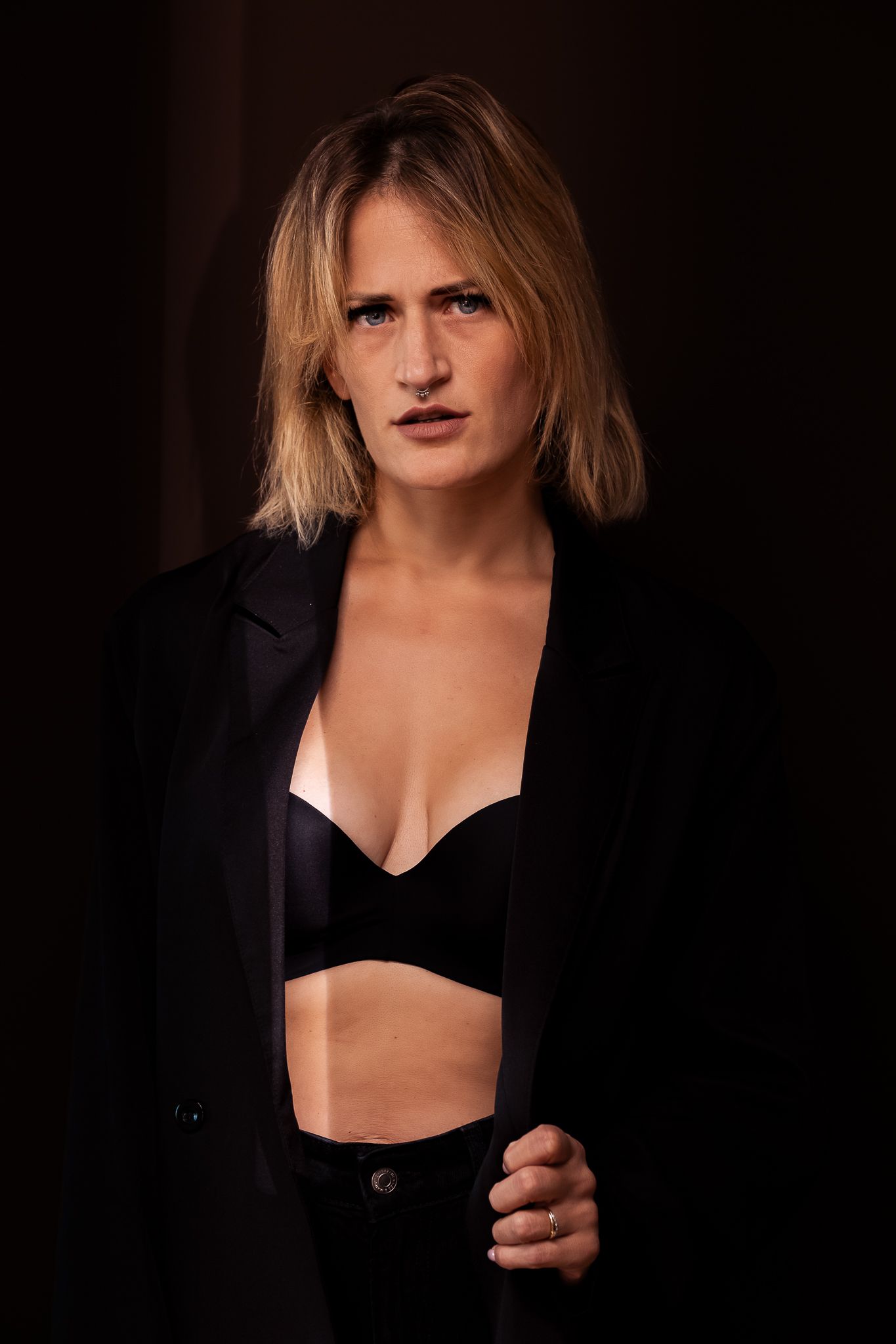 Dramatic portrait series in black blazer against dark background.