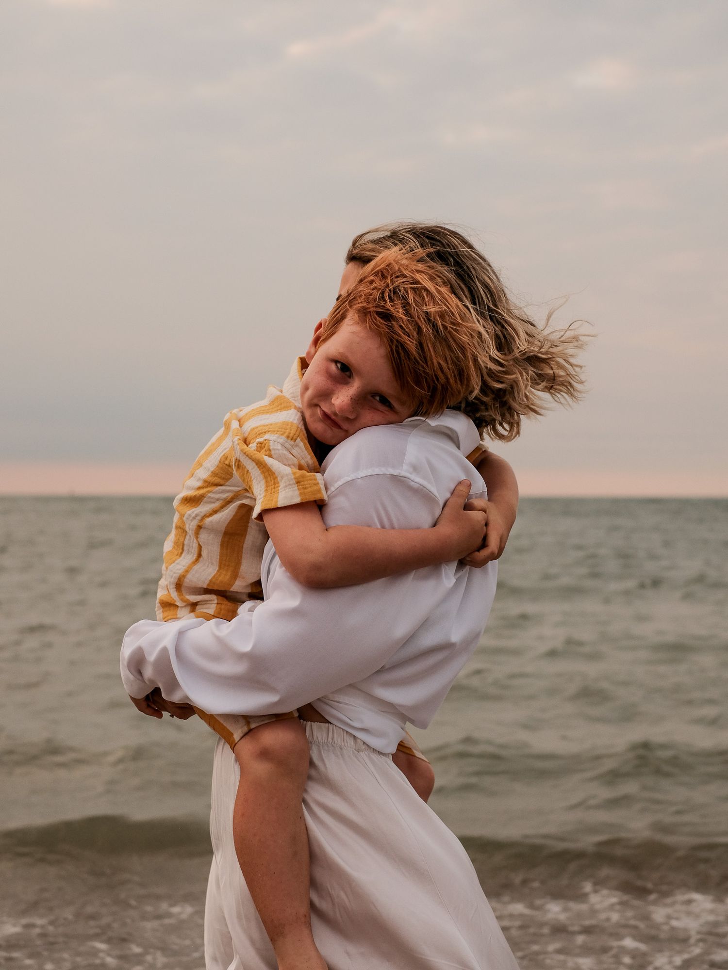 Emotional embrace captured at sunset against ocean backdrop.