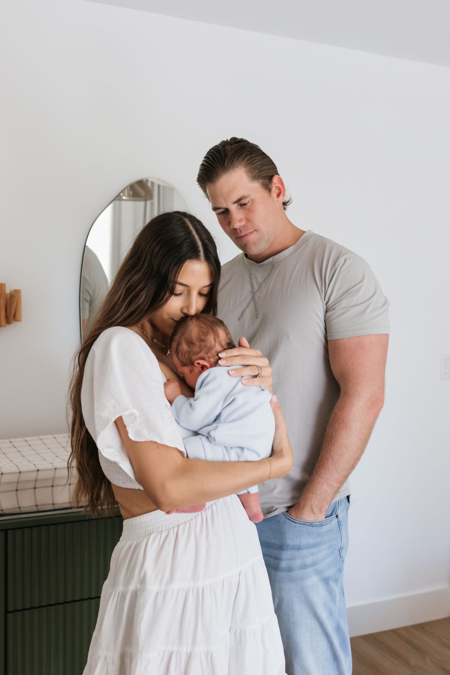 A couple tenderly cradles their newborn baby in a bright, modern bathroom setting.
