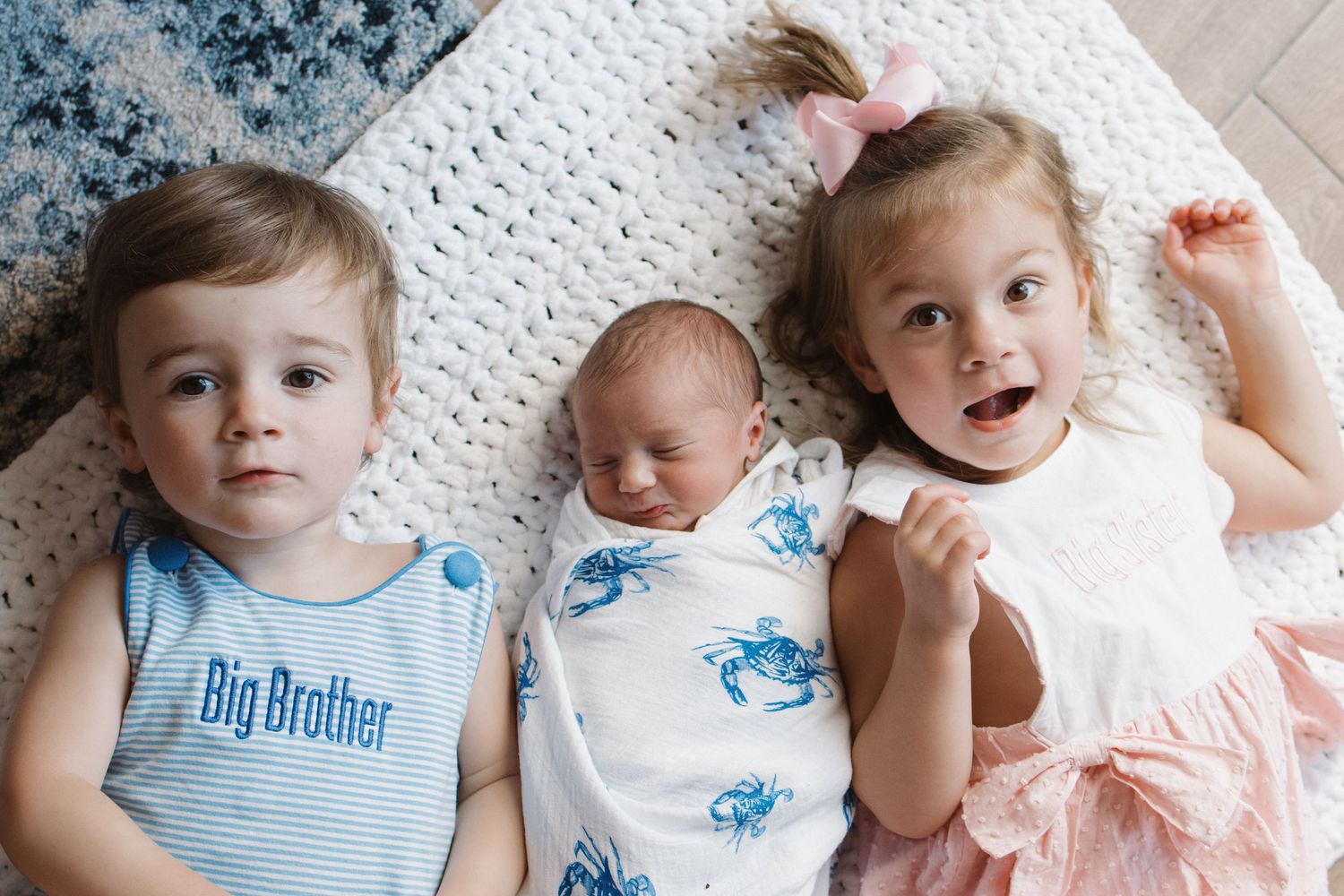Two young children in blue and white outfits lying together on a textured white blanket.