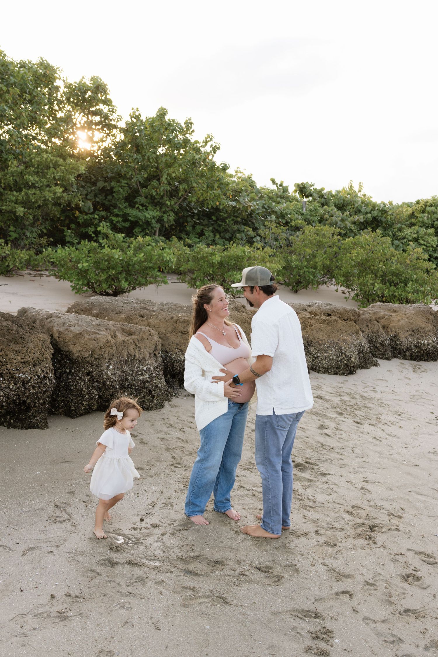 Family enjoying a playful moment on the beach with green foliage in background.