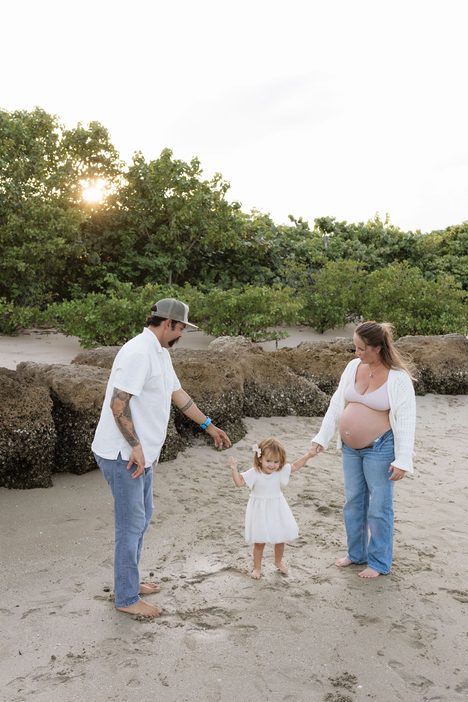 A family plays together on a sandy beach at sunset.