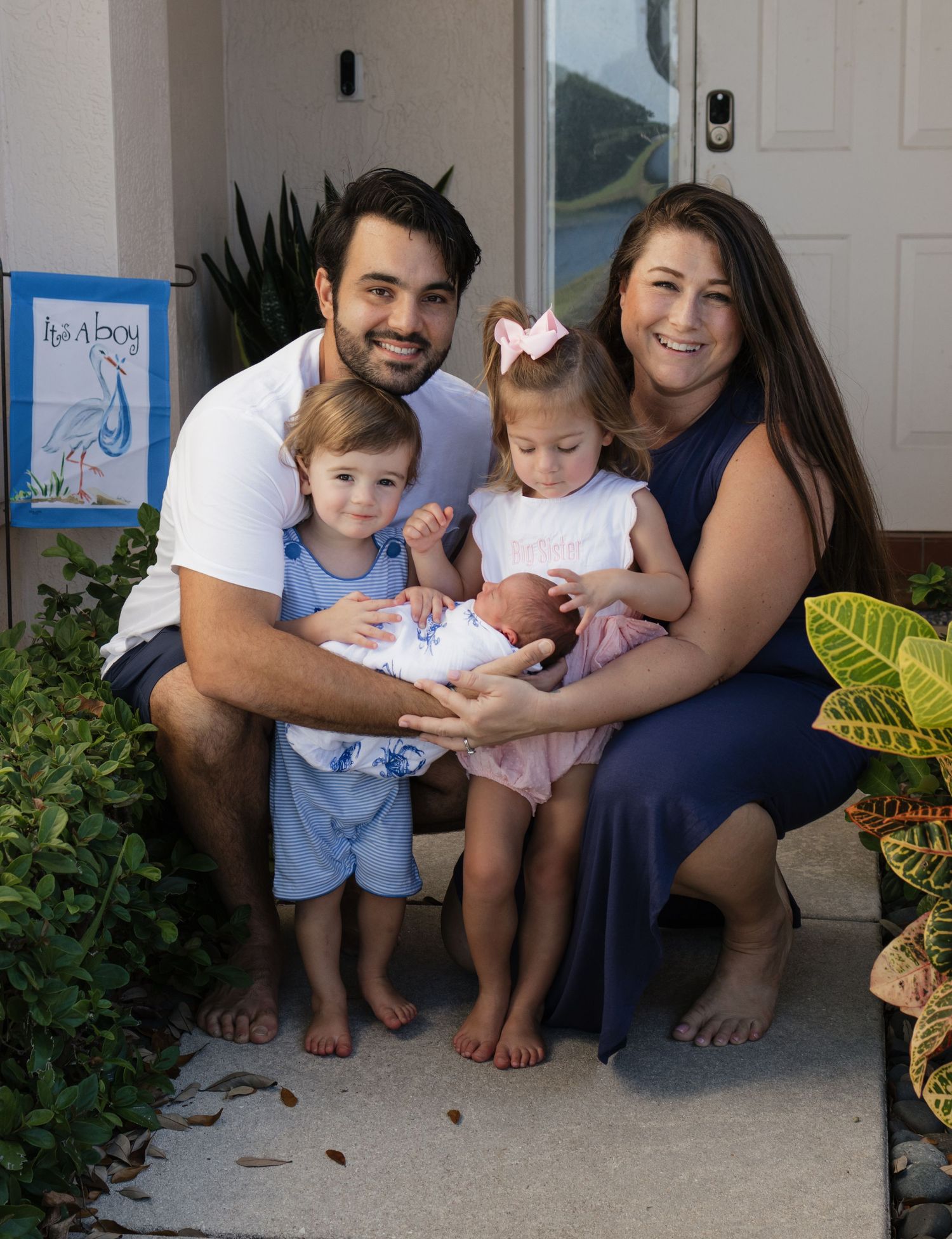 Family sitting together on a front porch with plants and decorative elements.