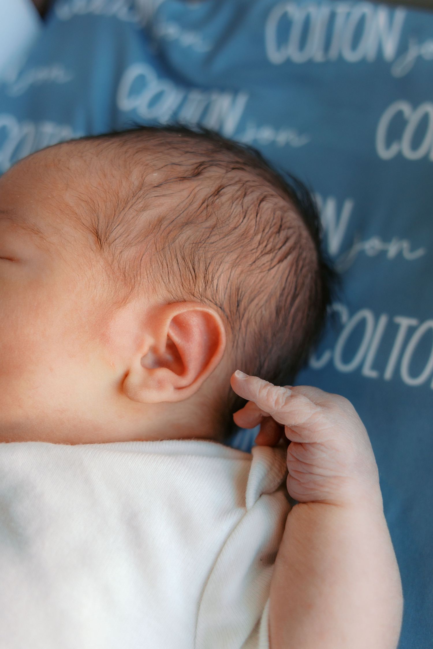 Newborn baby Colton sleeping peacefully on a personalized blue name blanket, showing delicate ear and tiny fingers.