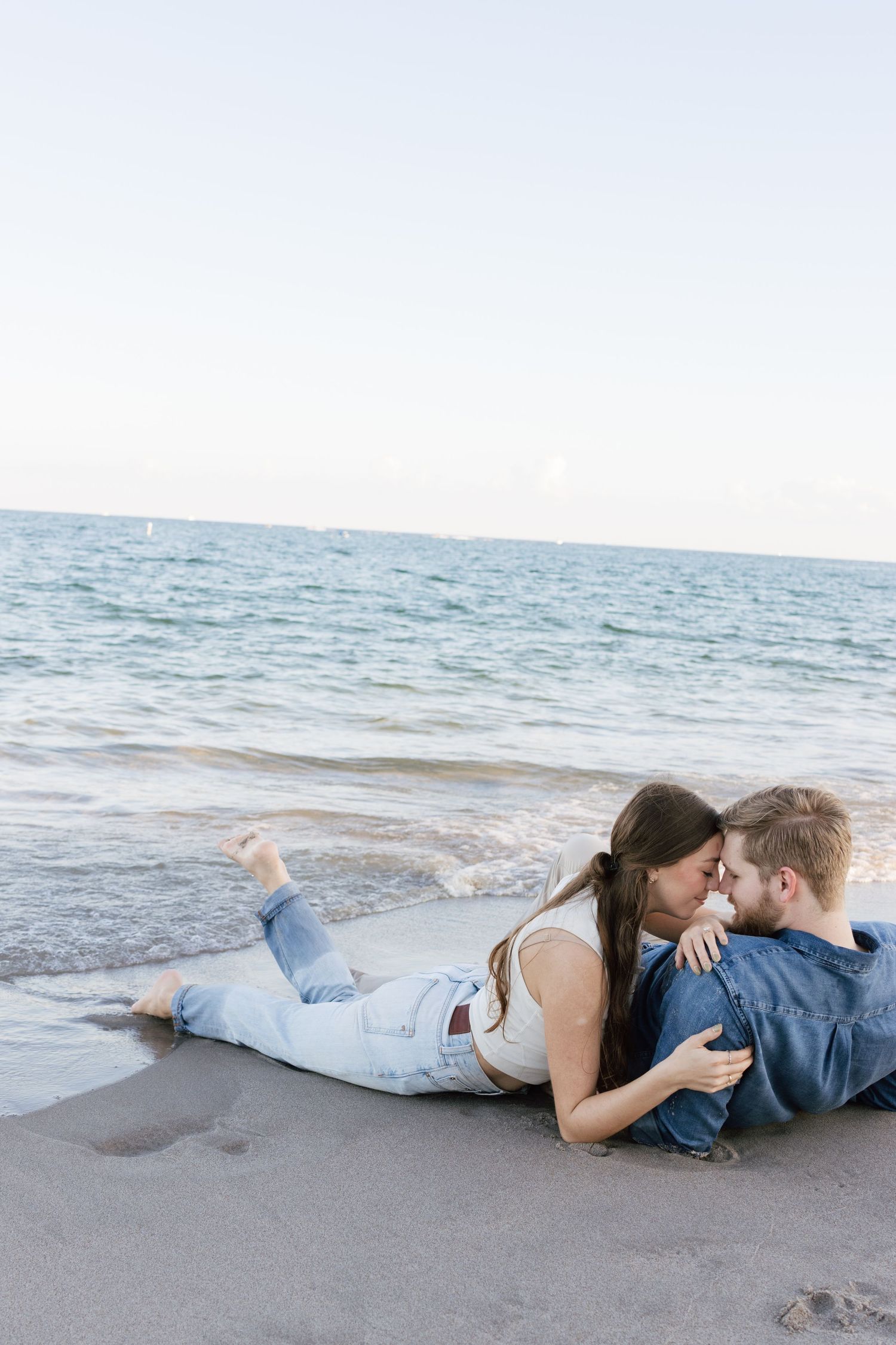 Romantic couple lying on beach near ocean waves at sunset.