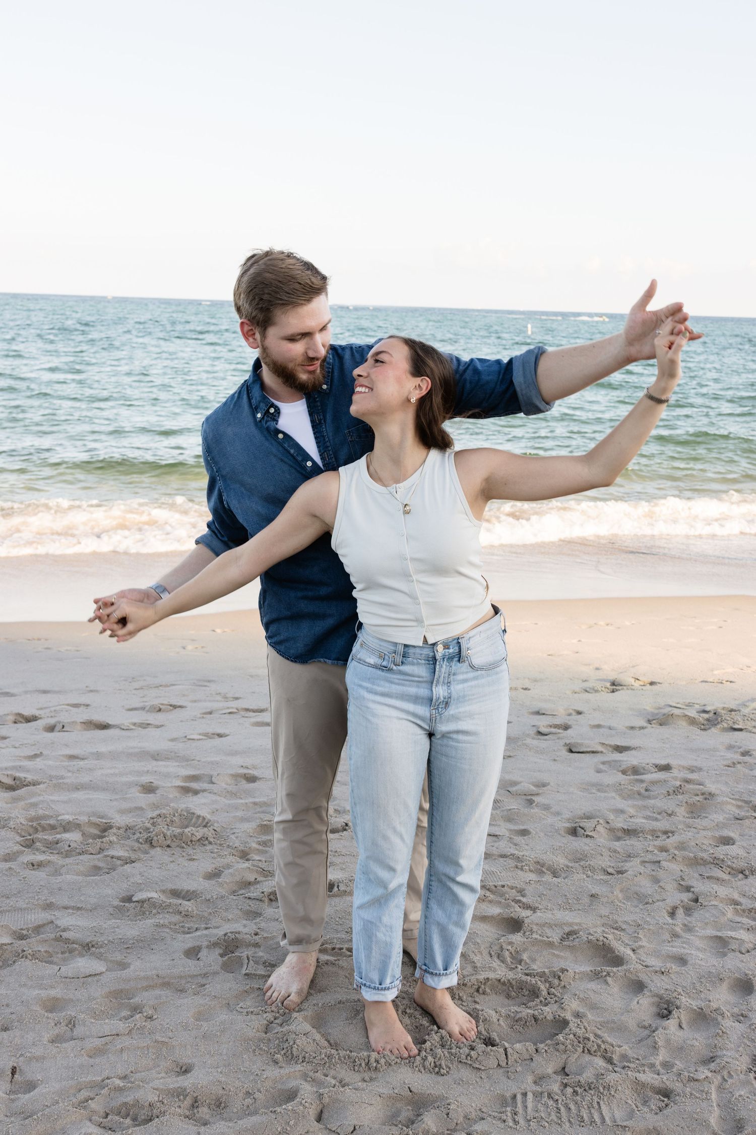 Joyful dancing moment captured on sandy beach with ocean backdrop.