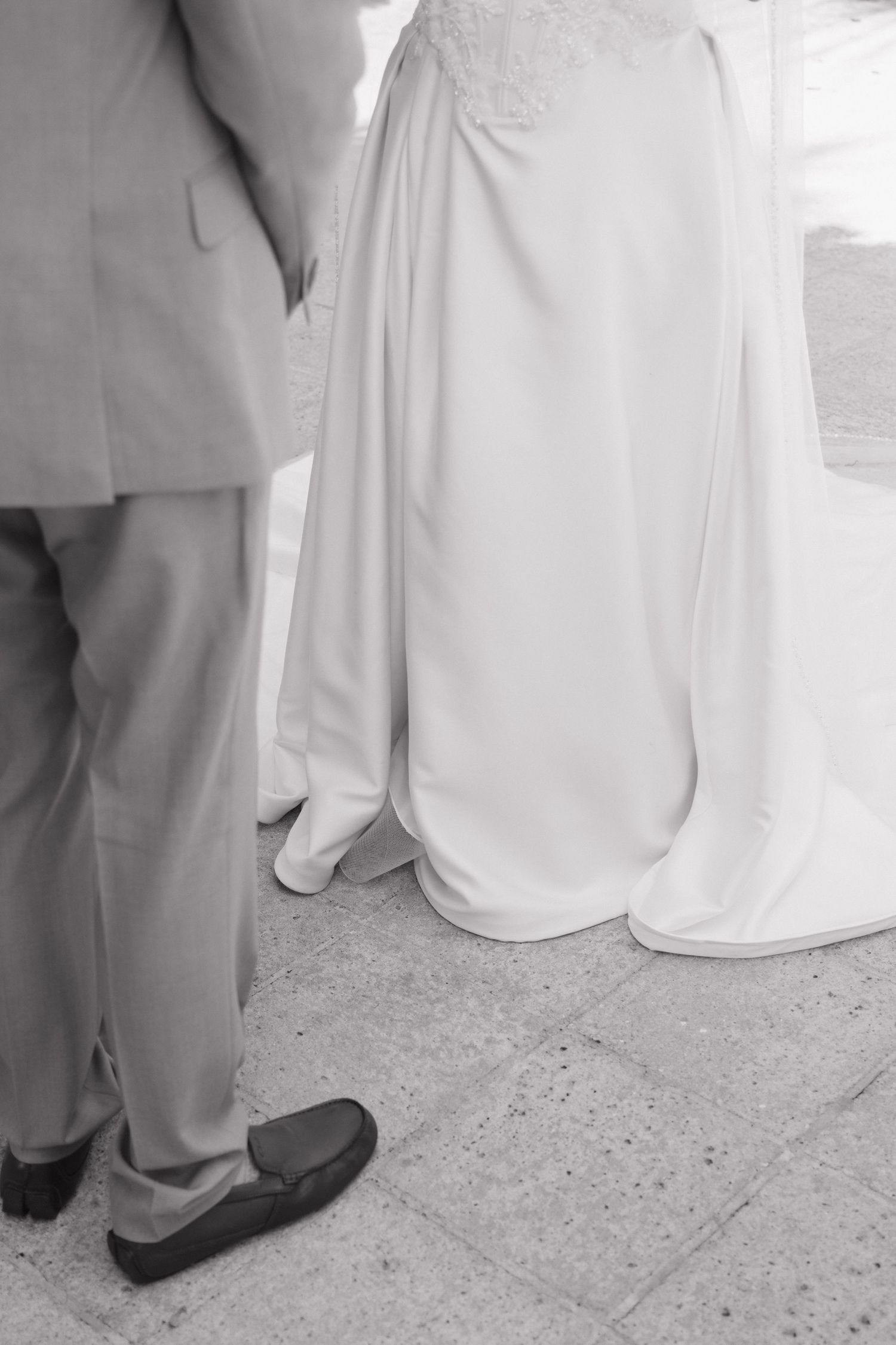 Black and white photo of bride in white gown and groom in beige suit standing together.