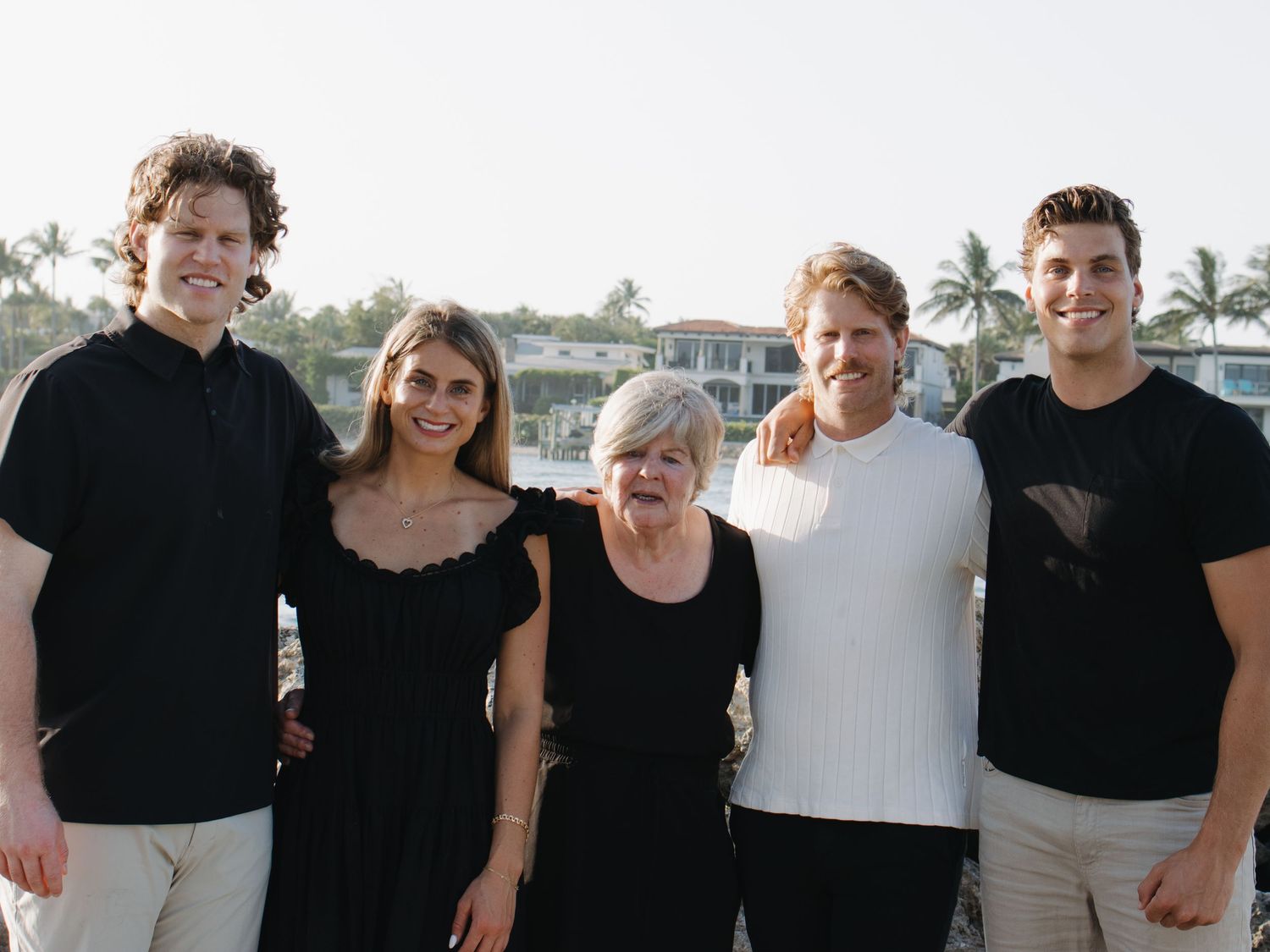 A group photo of five people wearing black and white outfits against a coastal backdrop.