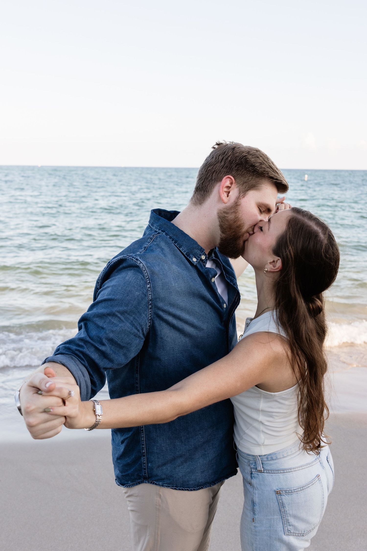 A couple dips and kisses during a romantic moment on a sandy beach.