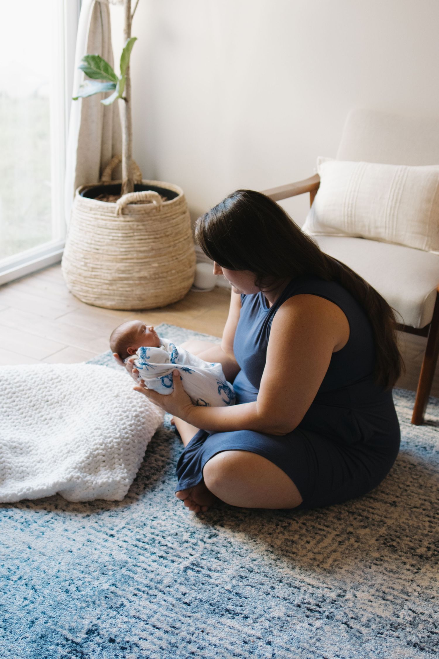 Mother laying on carpet while tending to baby on white blanket.