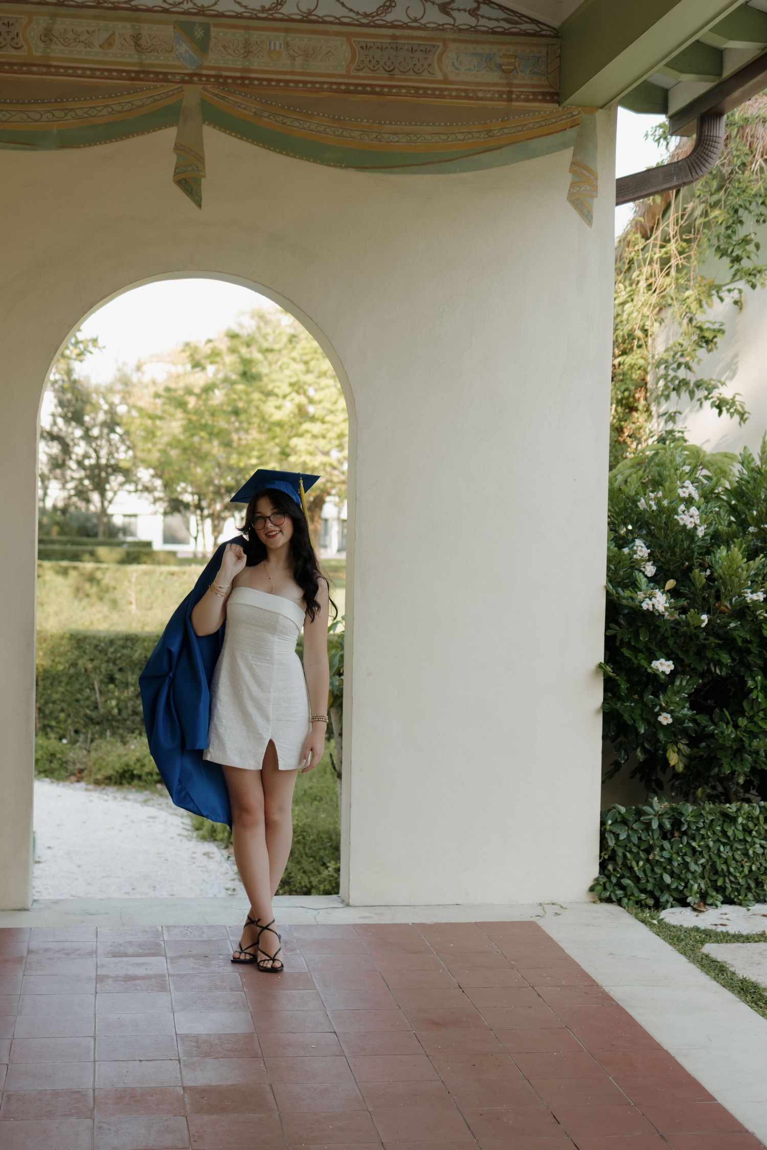 Graduate takes photos under covered walkway with arched columns.
