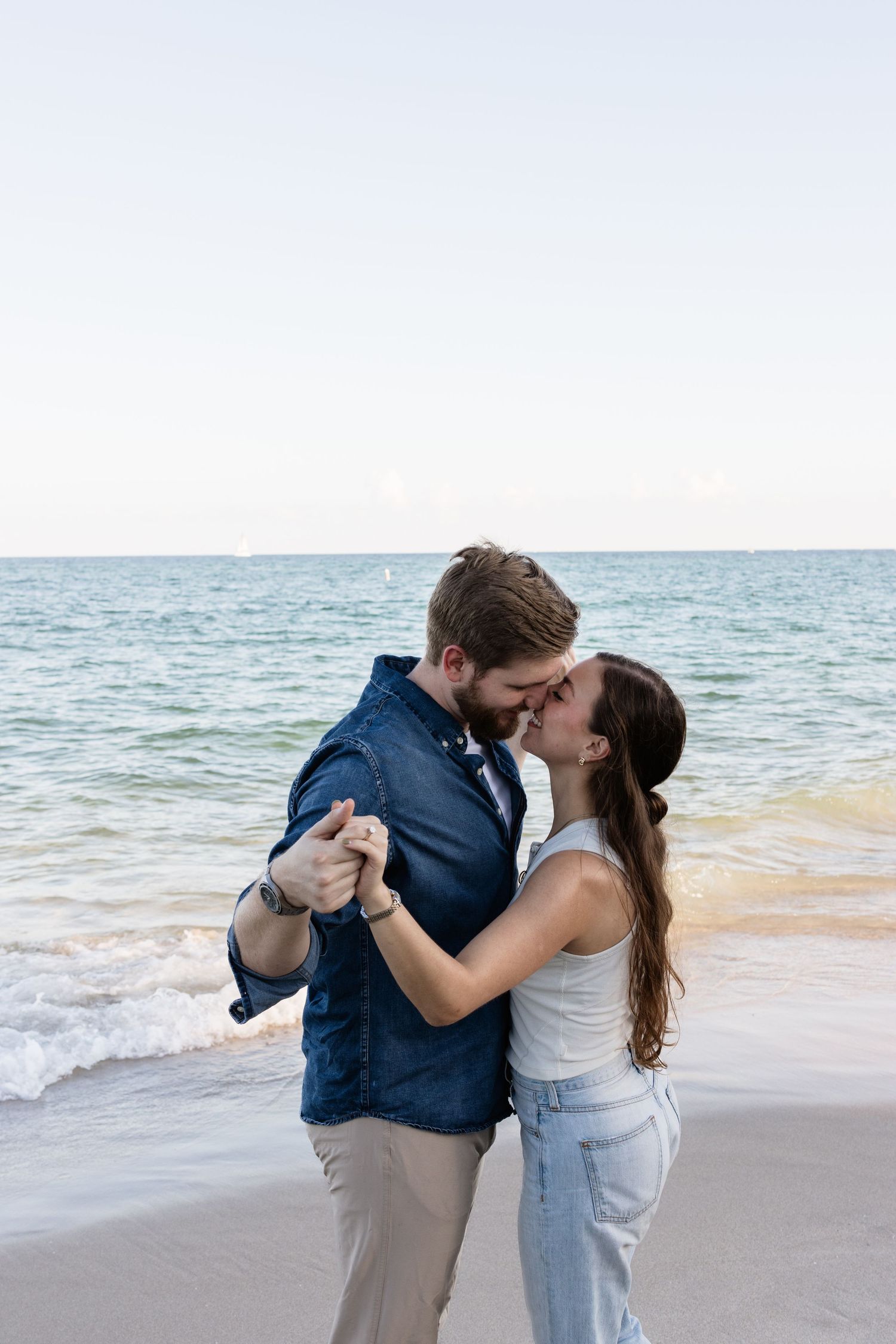 Two people embrace in a romantic dance pose along the ocean shoreline.