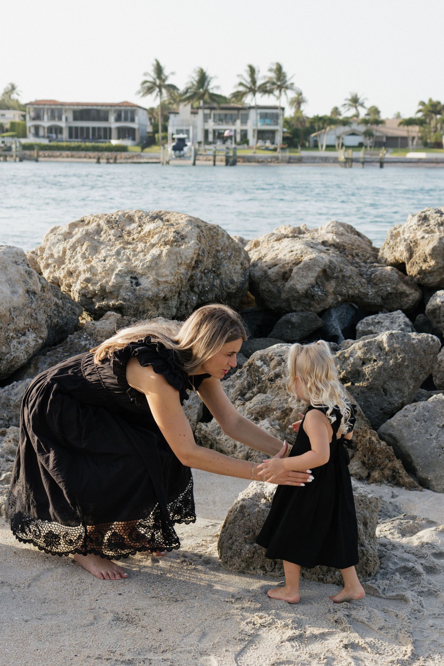 A tender moment between parent and child playing on a rocky beach with waterfront homes visible.