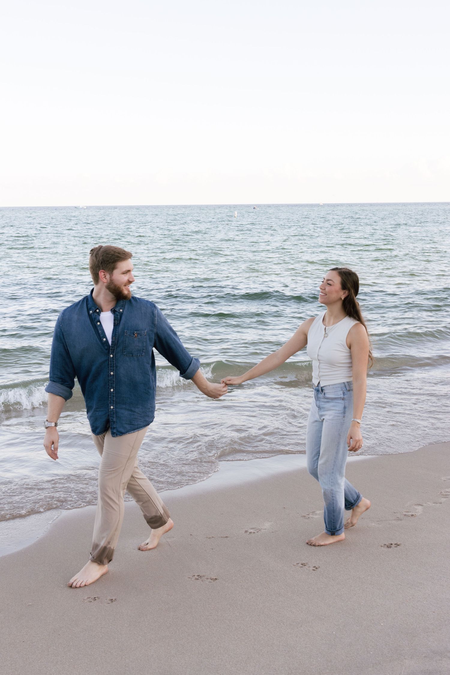 Playful couple running and holding hands along the ocean shoreline.