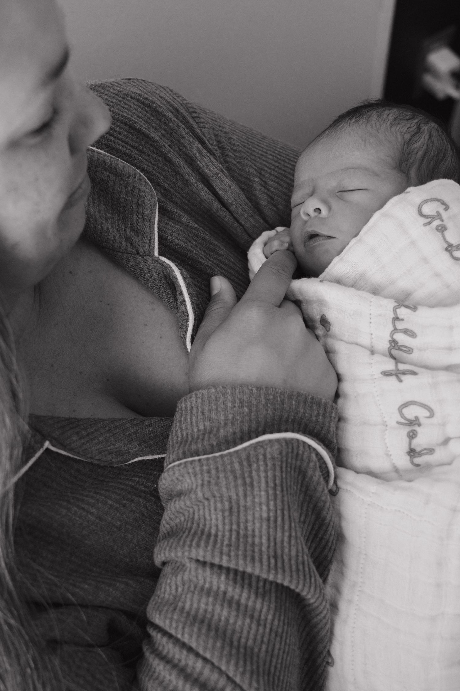 Black and white photo of a parent cradling a sleeping newborn baby wrapped in a white blanket.