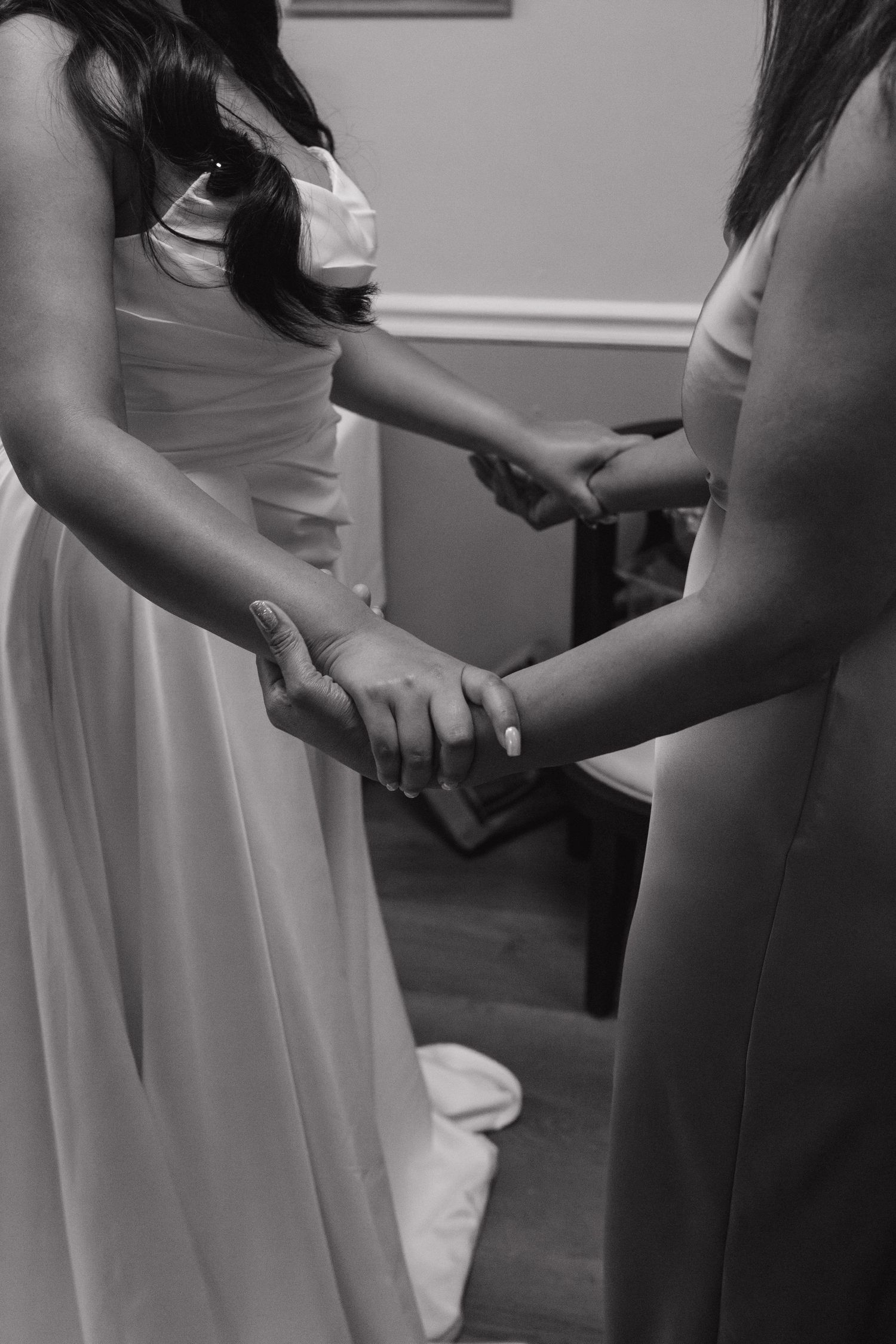 Black and white photo of bride and bridesmaid holding hands during wedding preparations.