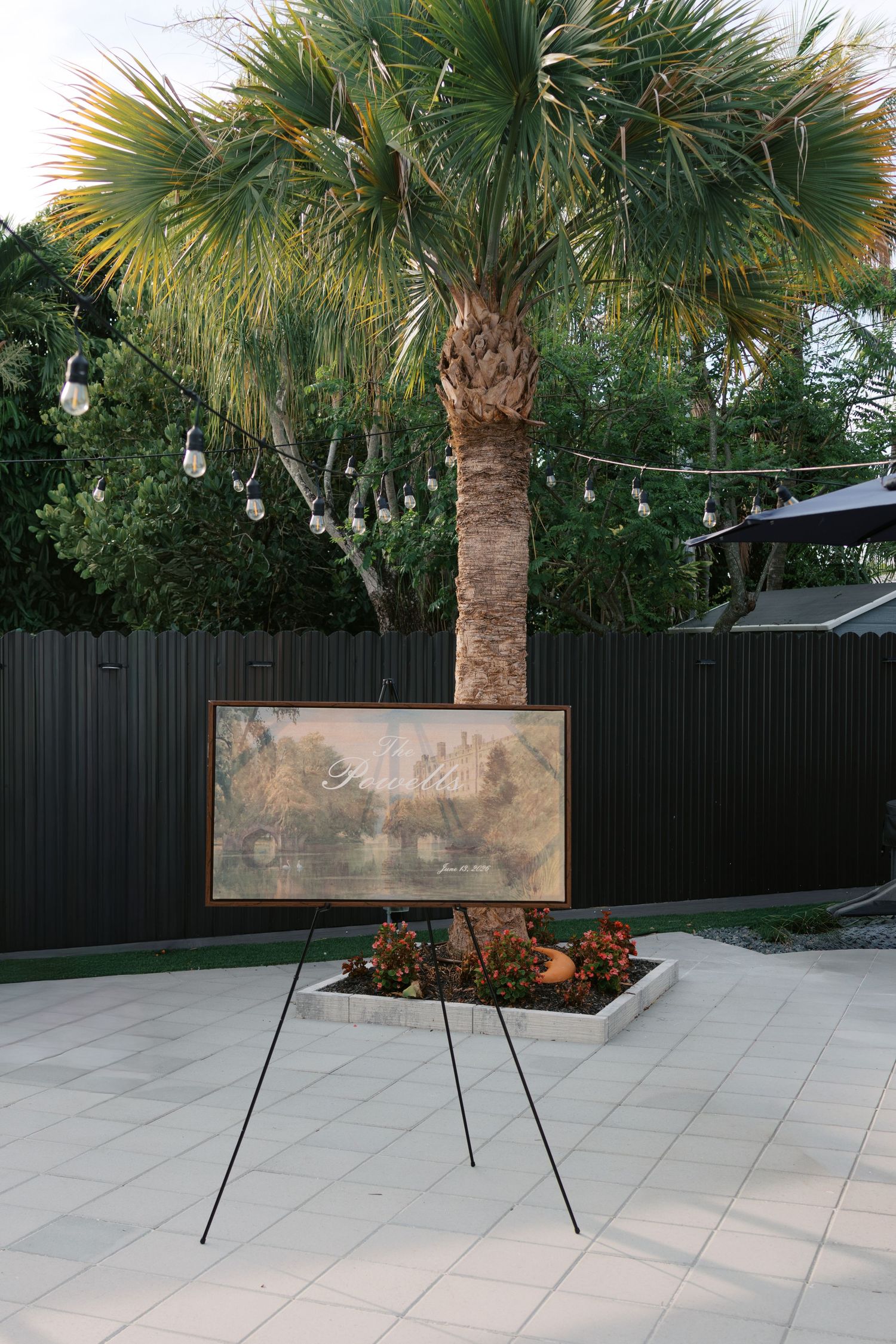 Elegant wedding welcome sign on easel displayed near a palm tree with string lights at dusk.